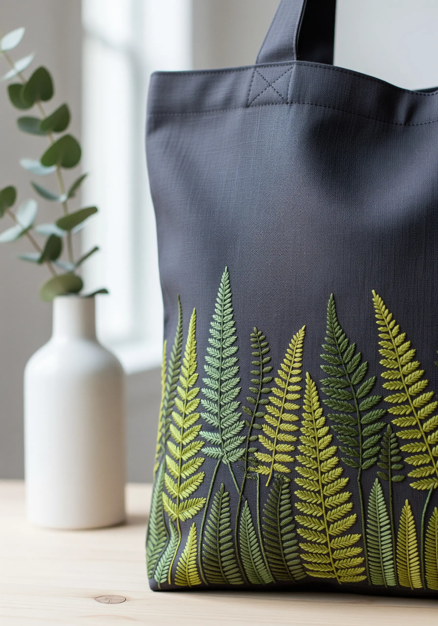 A dense border of embroidered ferns in shades of green along the bottom of a dark tote bag