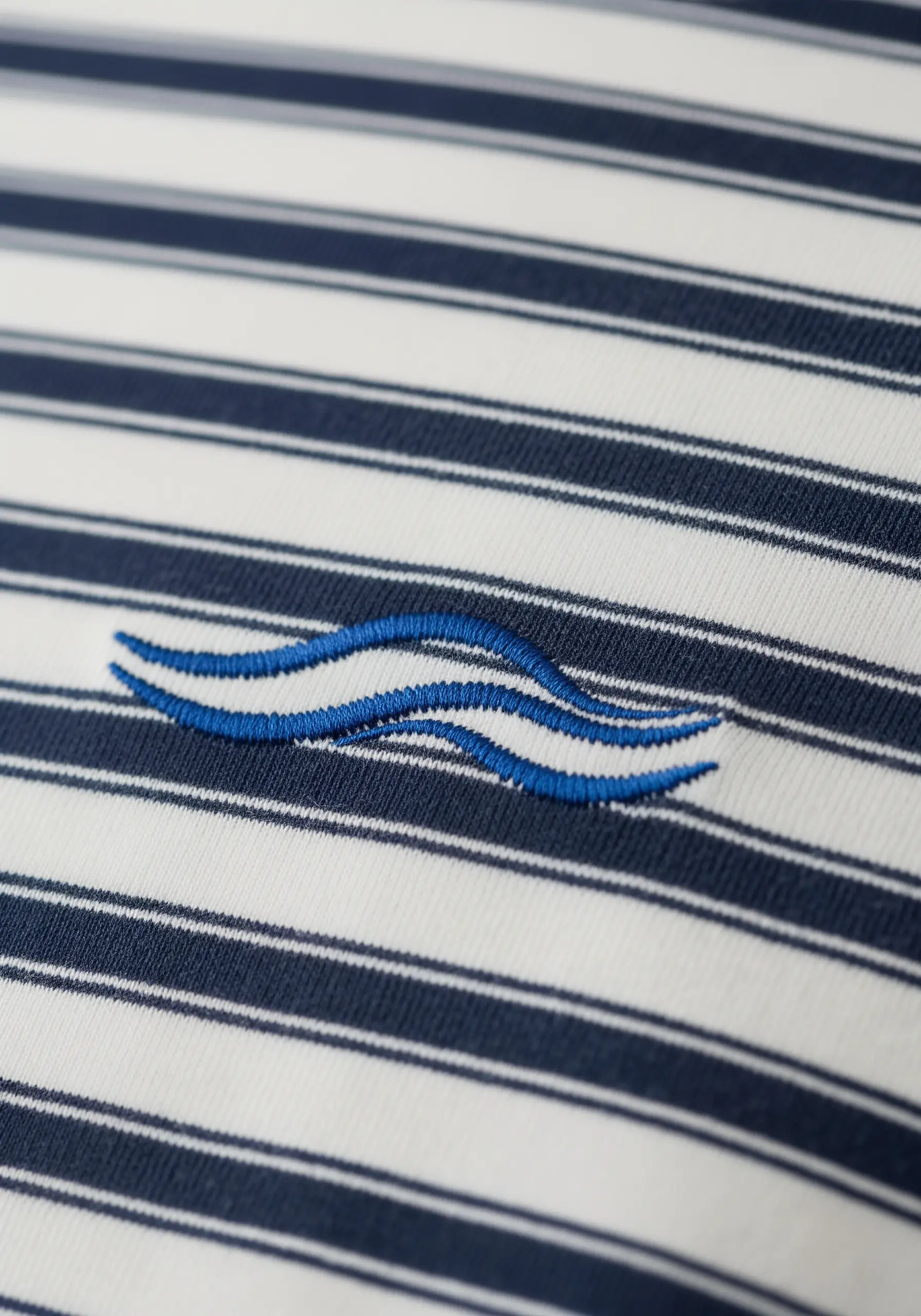 Abstract blue waves embroidered over a navy and white striped polo shirt.