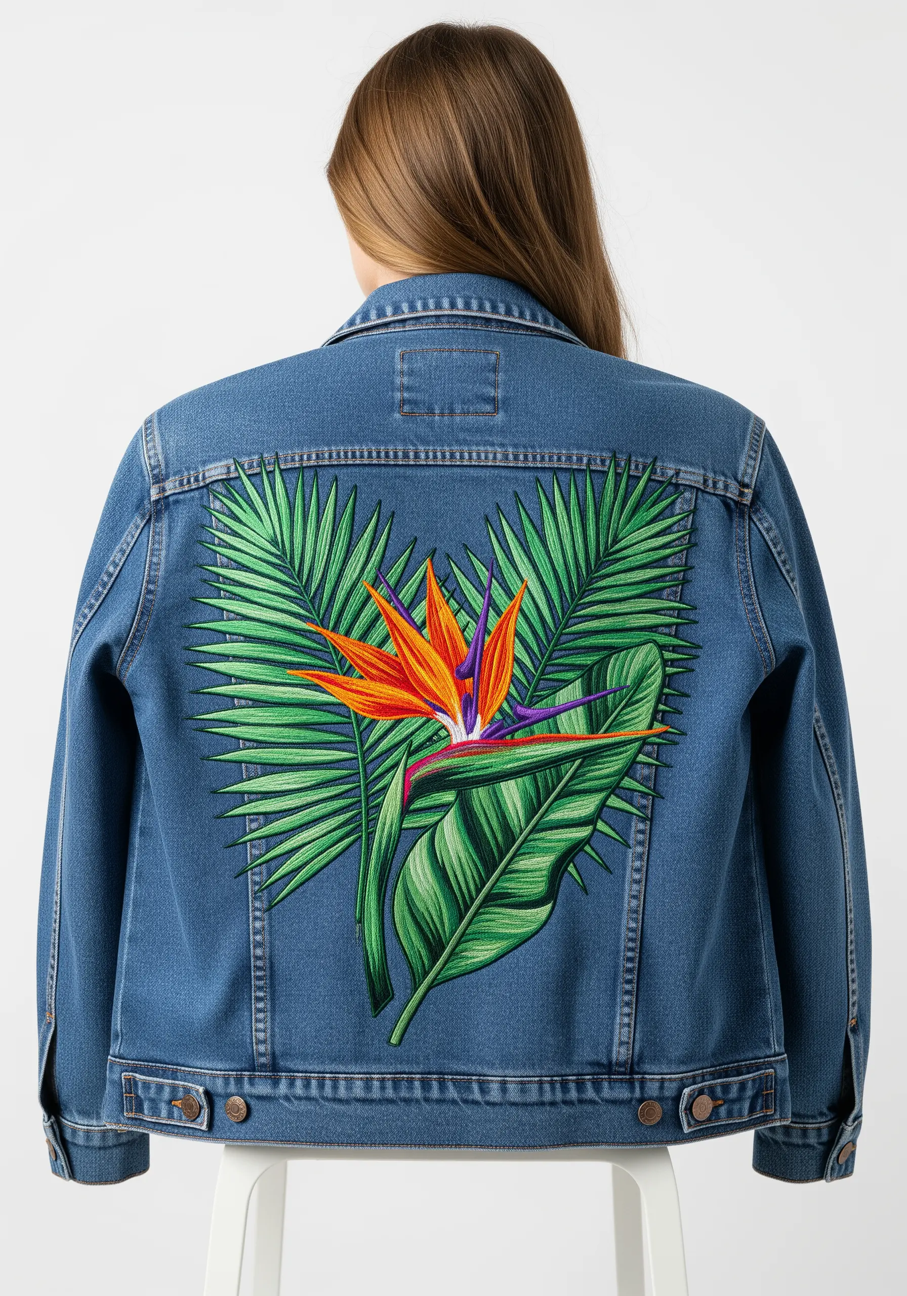 Vibrant Bird of Paradise and palm leaves embroidered on the back of a denim jacket.