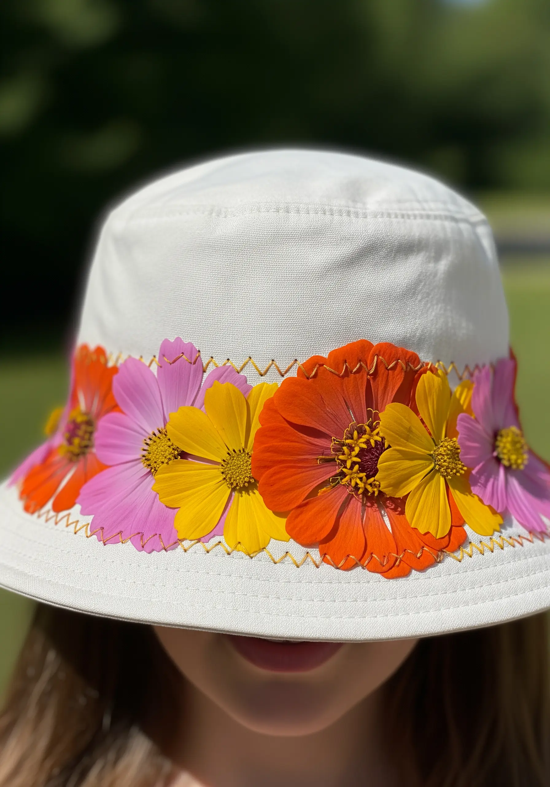A white sun hat with a colorful band of real pressed zinnia flowers held by gold thread.