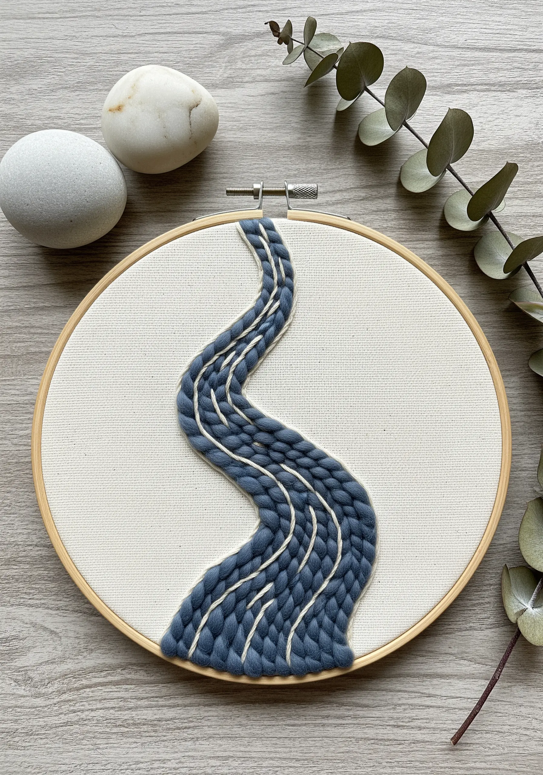 Abstract river shape made with thick blue yarn couched onto cream fabric in a hoop.