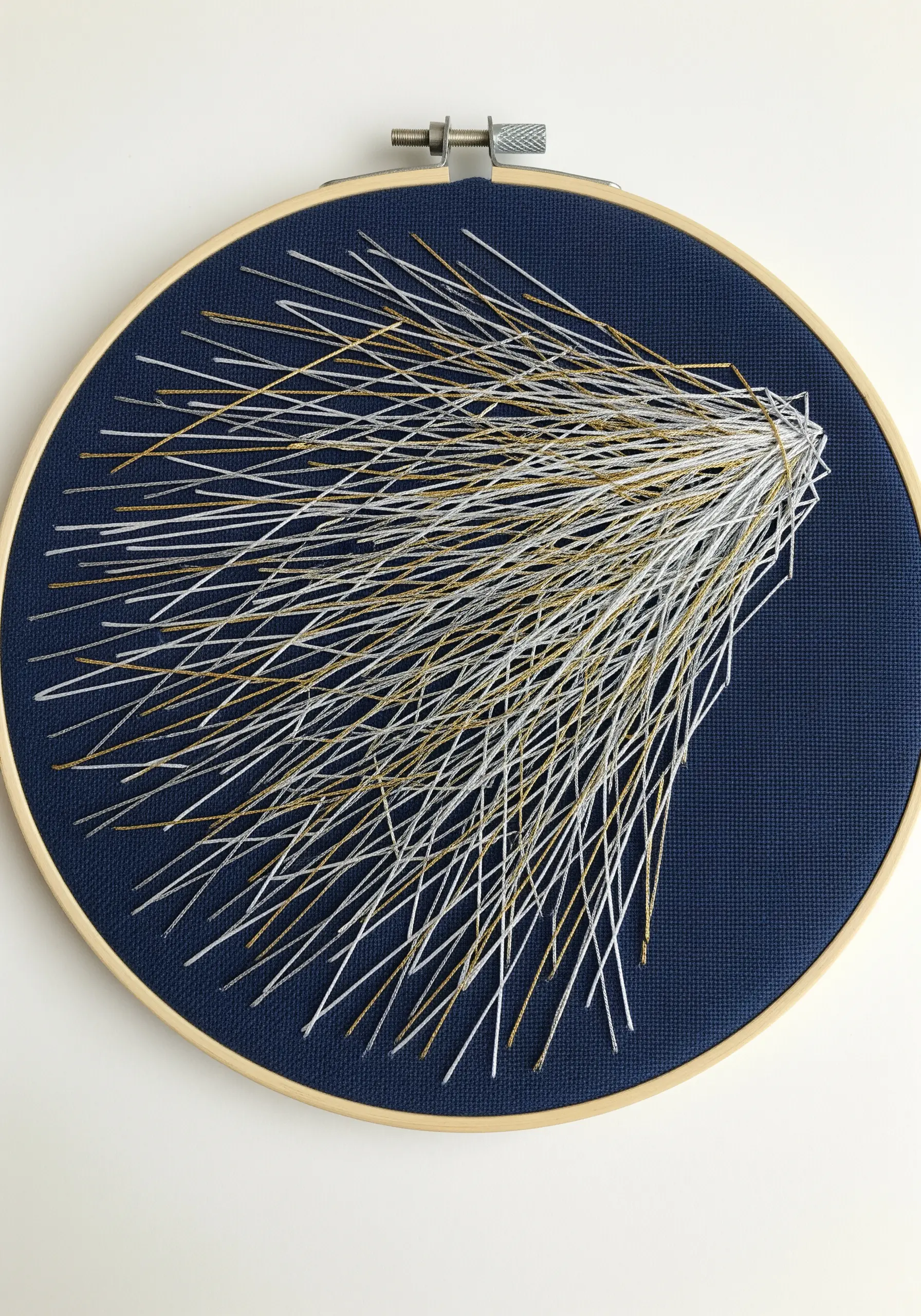 Abstract burst of white and gold straight stitches on dark blue fabric in a hoop
