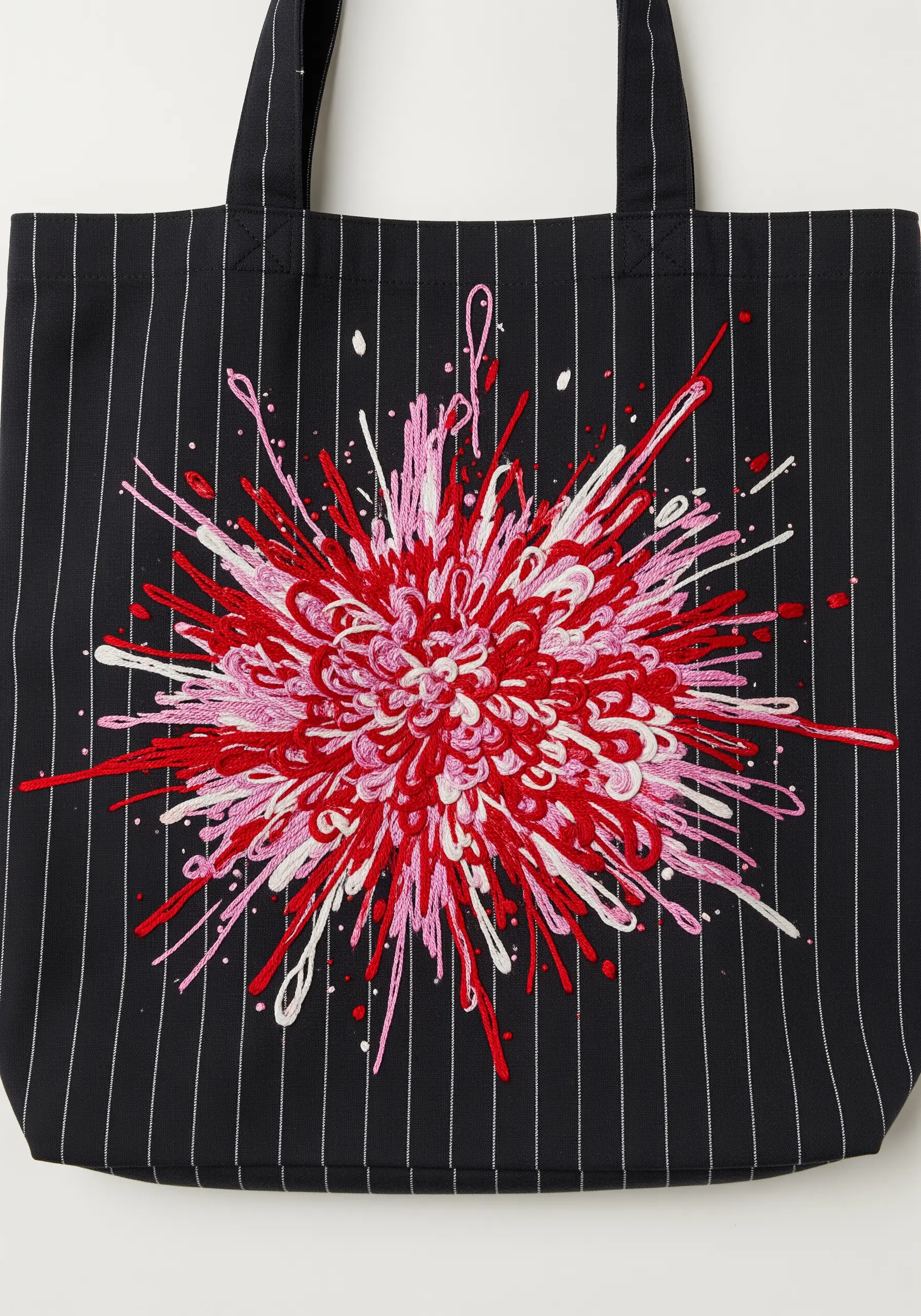 An abstract explosion of pink and red threads on a pinstripe tote bag.