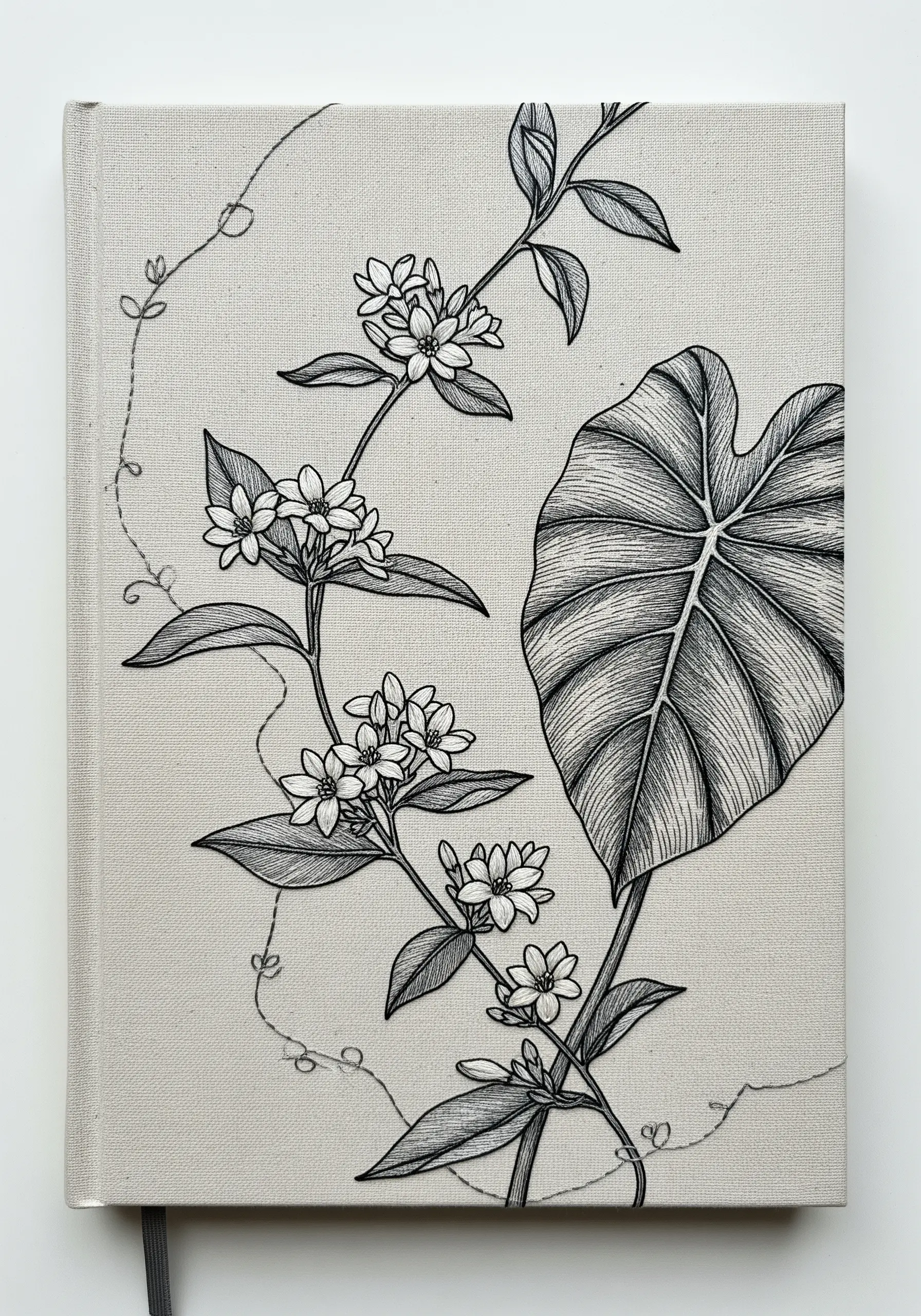 Black thread line art embroidery of flowers and a large leaf on a linen book cover.