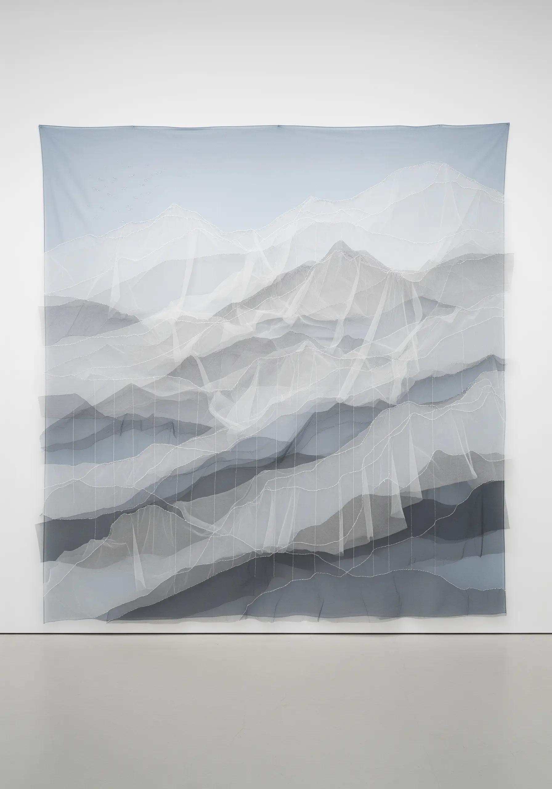 Large wall hanging of a mountain range made from layered sheer grey and white fabrics with visible stitches.