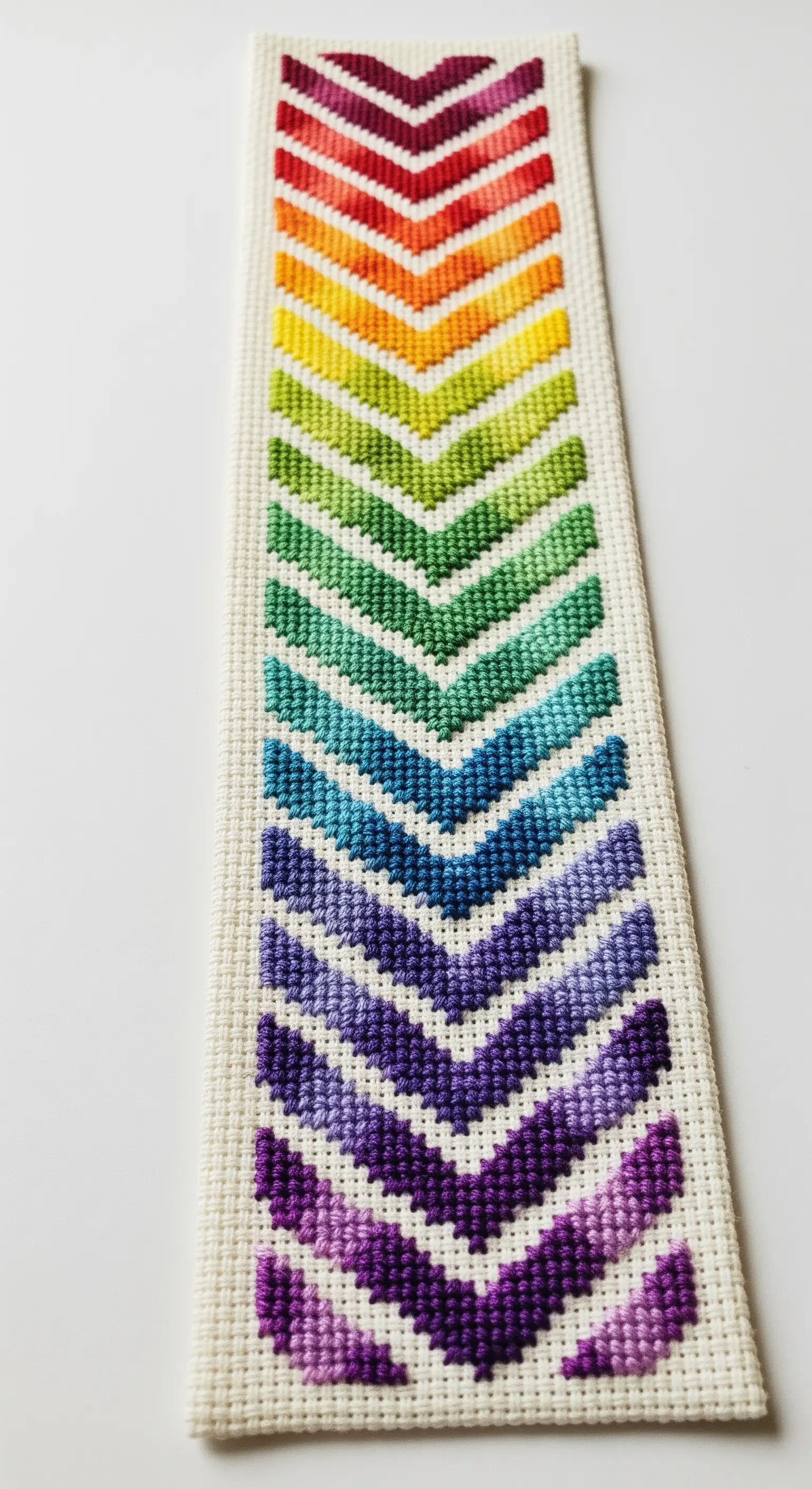 A bookmark with a sharp rainbow chevron pattern using a counted stitch technique.