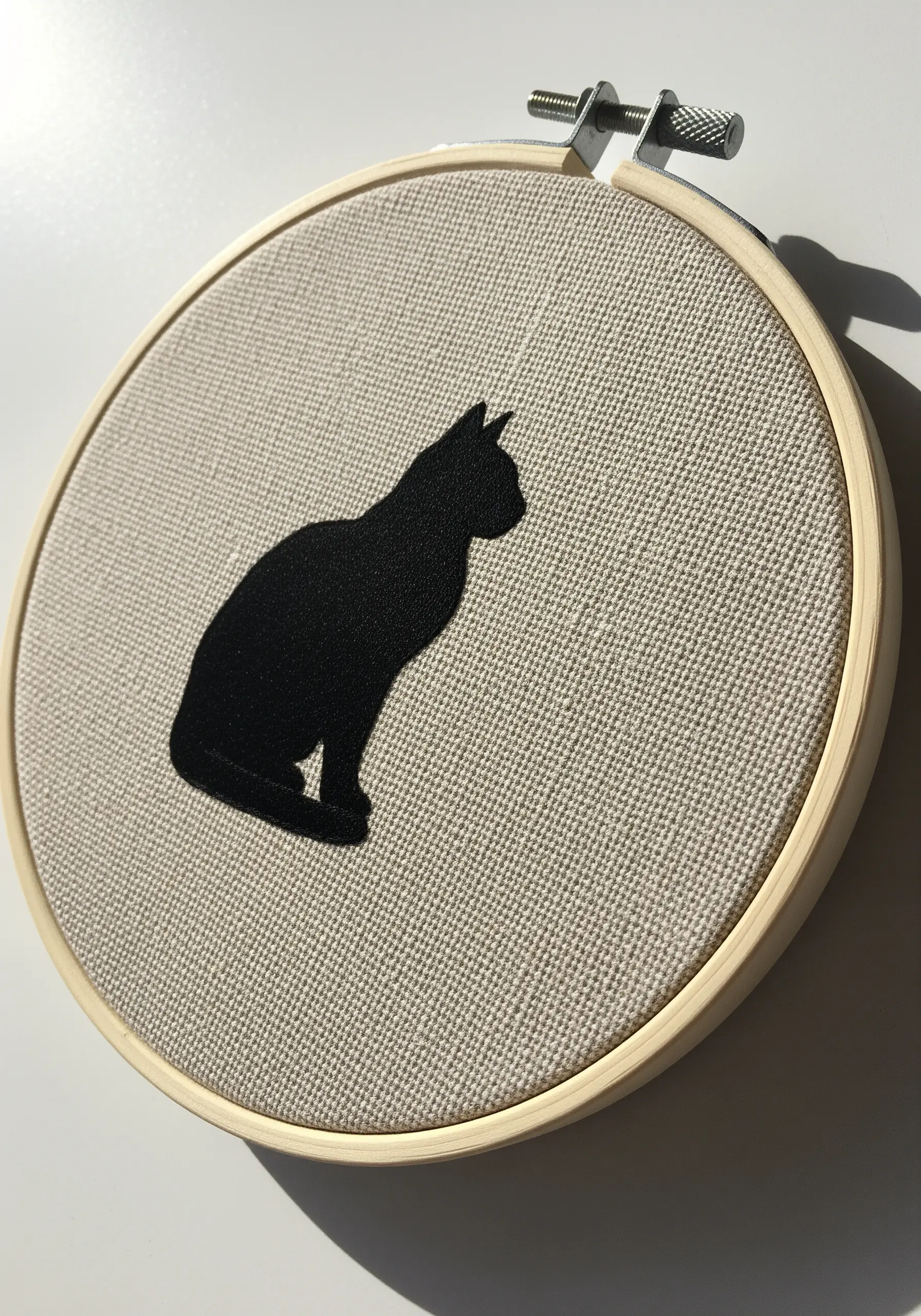 A crisp black silhouette of a sitting cat appliquéd onto a neutral linen background.