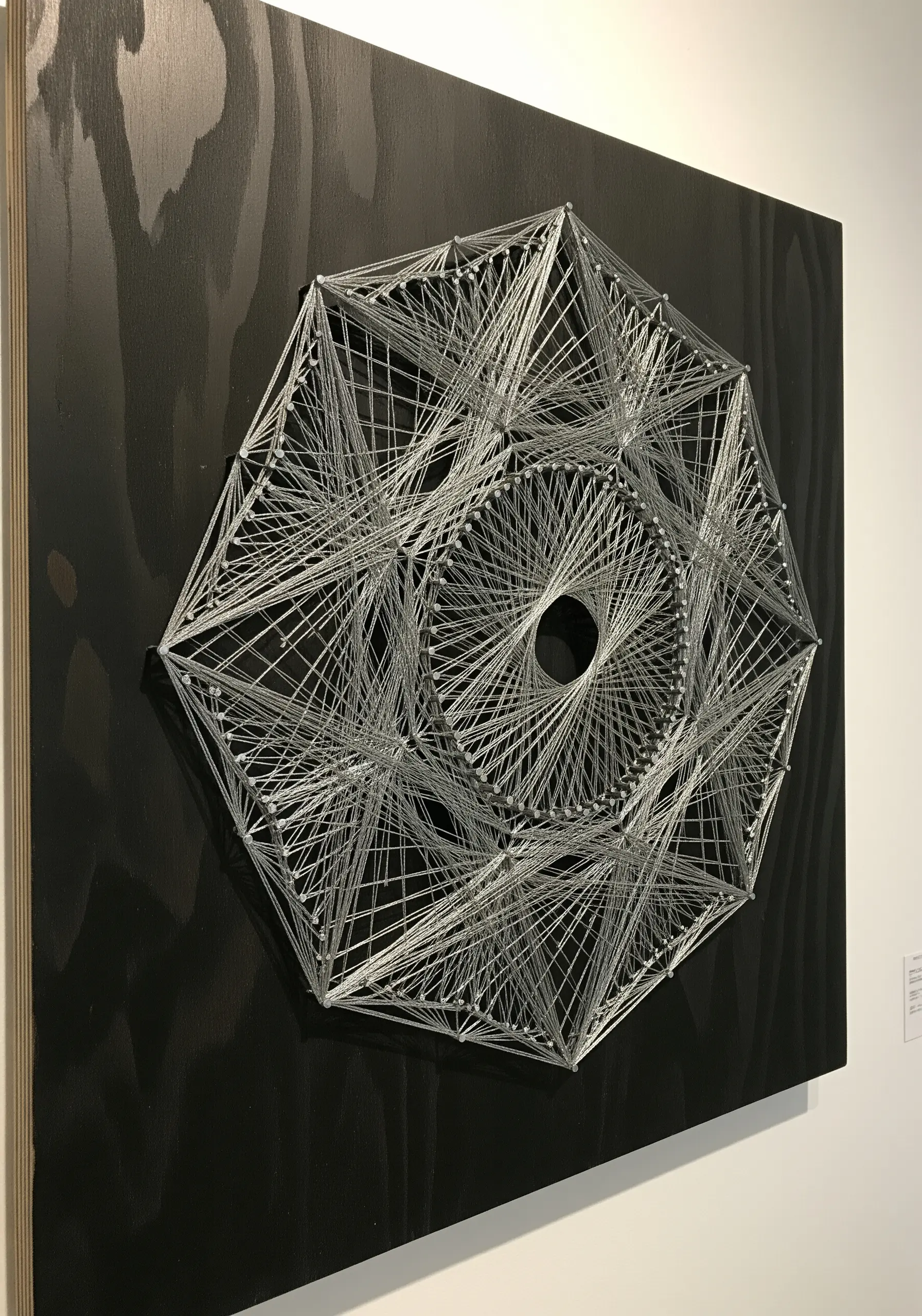 Monochromatic geometric string art made with white thread on a black wooden board.