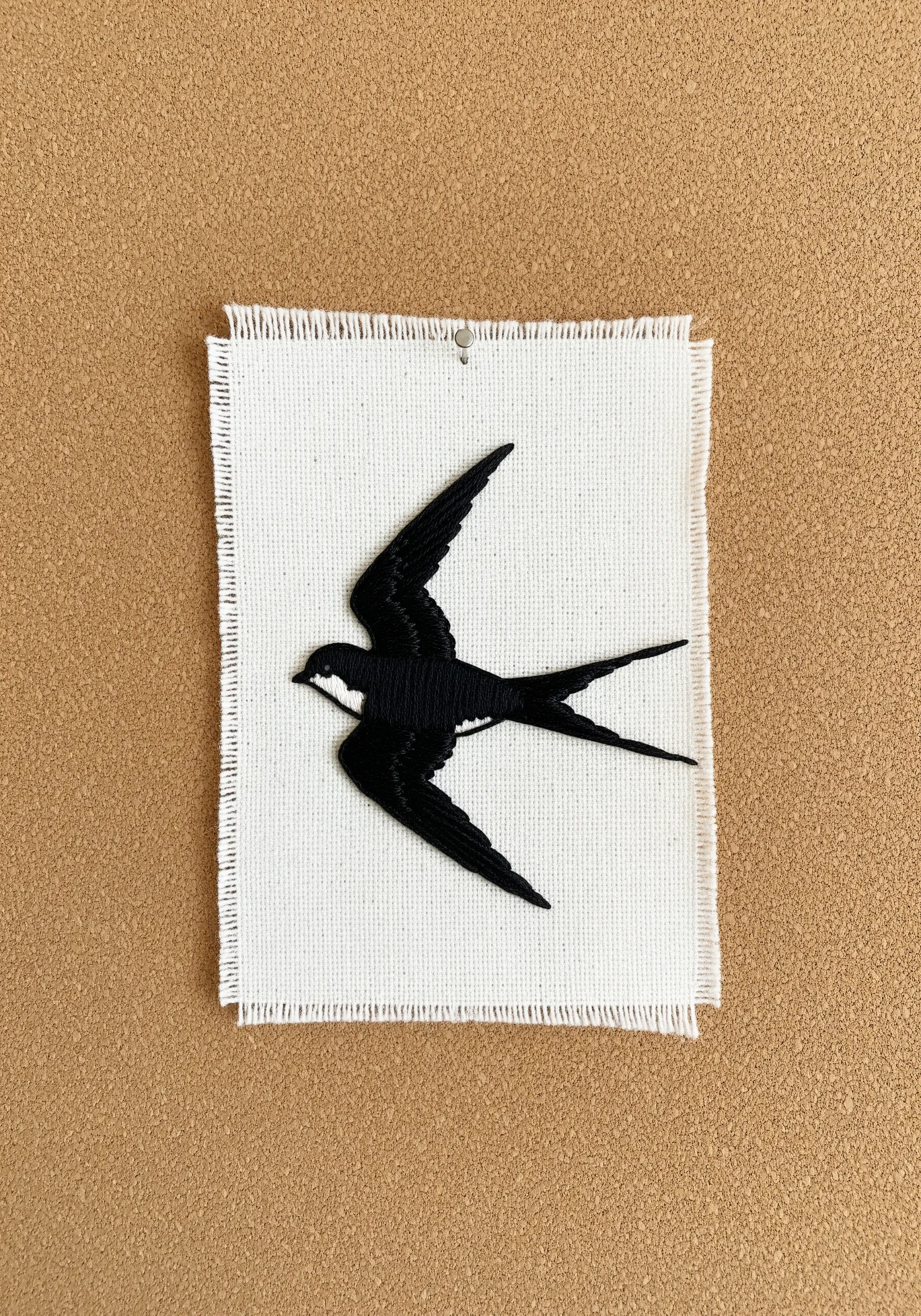 Solid black embroidered swallow silhouette on a raw-edged piece of white fabric.