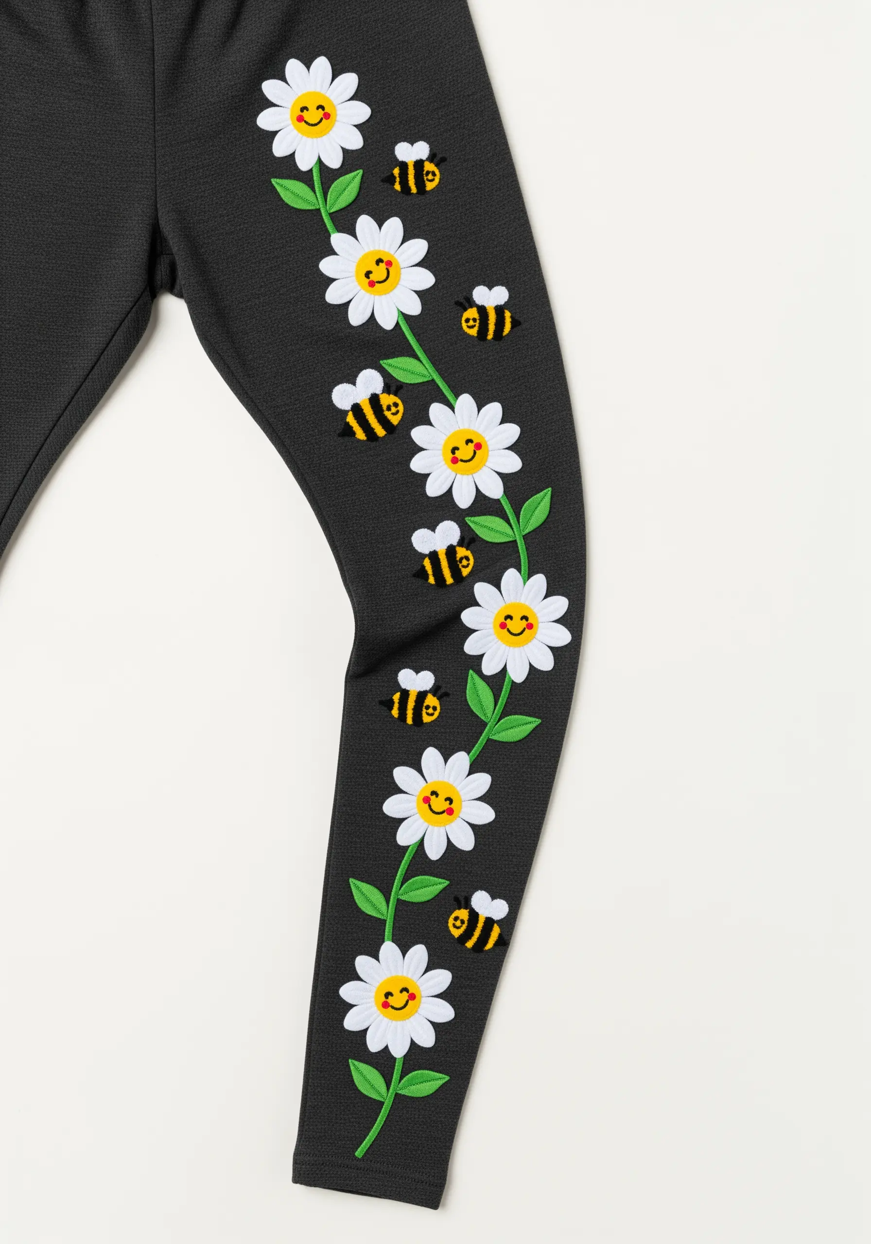 A vine of smiling daisies and bees embroidered up the side of a pair of dark grey leggings