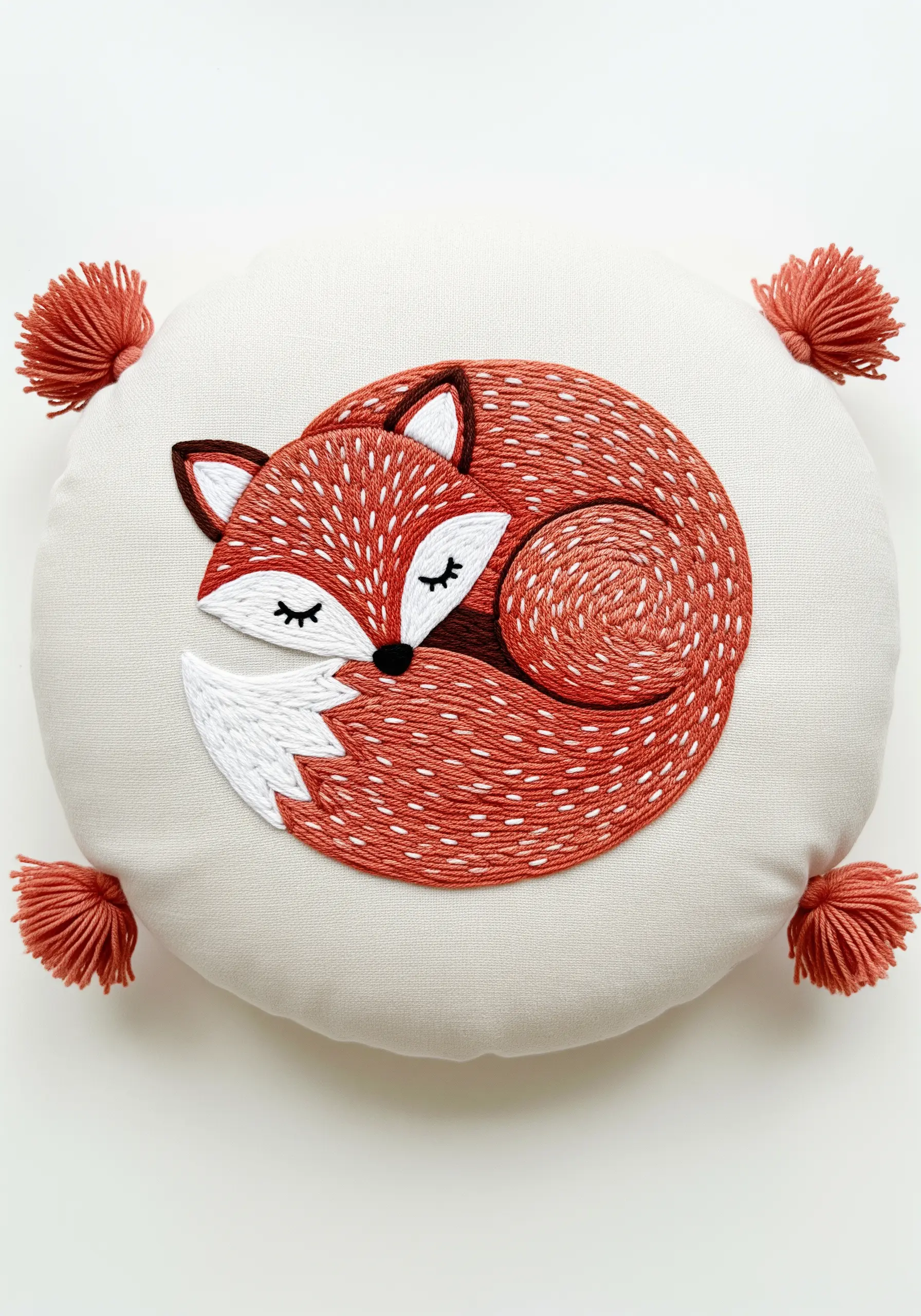 Embroidered sleeping fox on a round cushion with directional seed stitch fur texture.