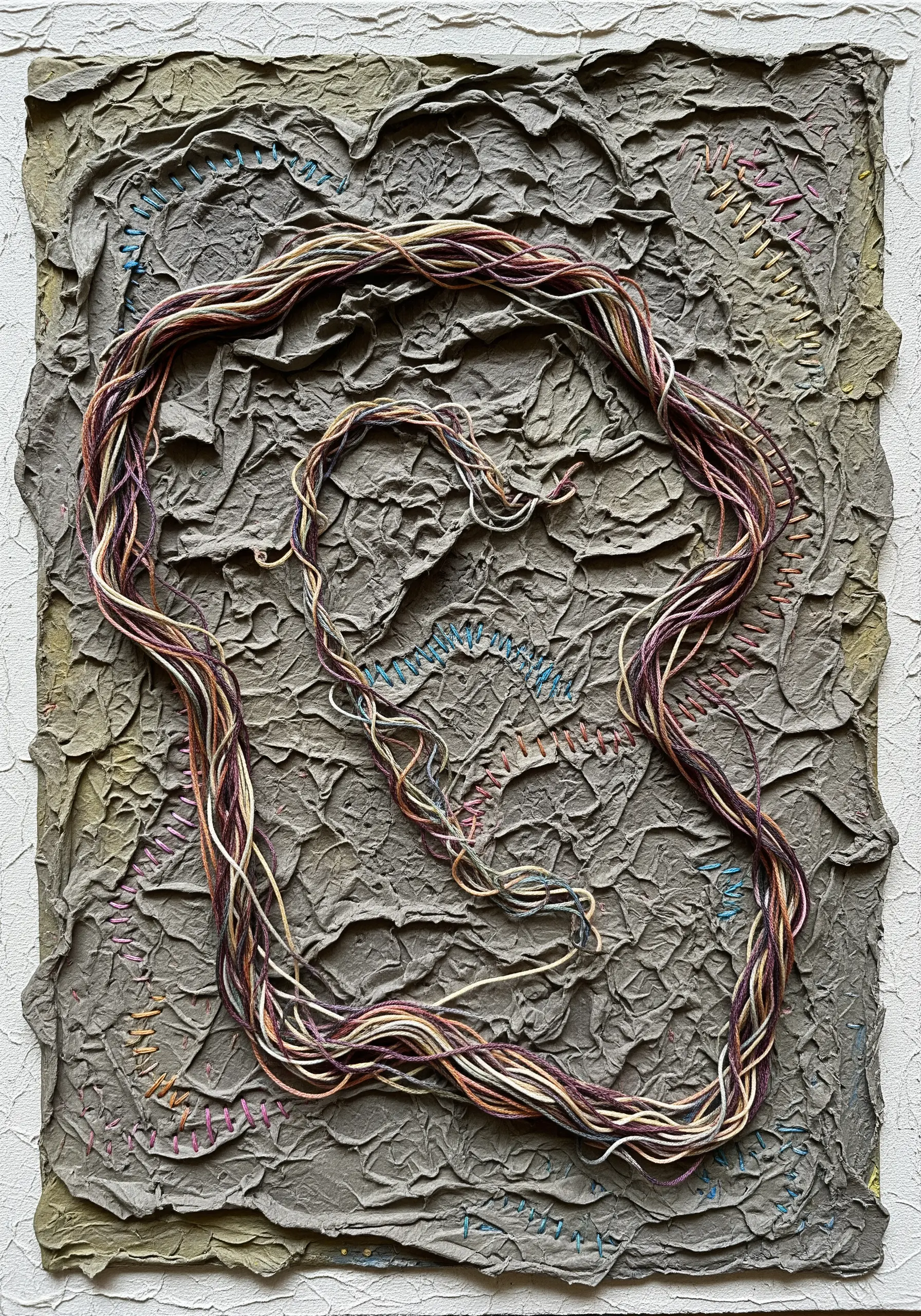 A highly textured abstract artwork made with gray papier-mâché and couched bundles of variegated thread.