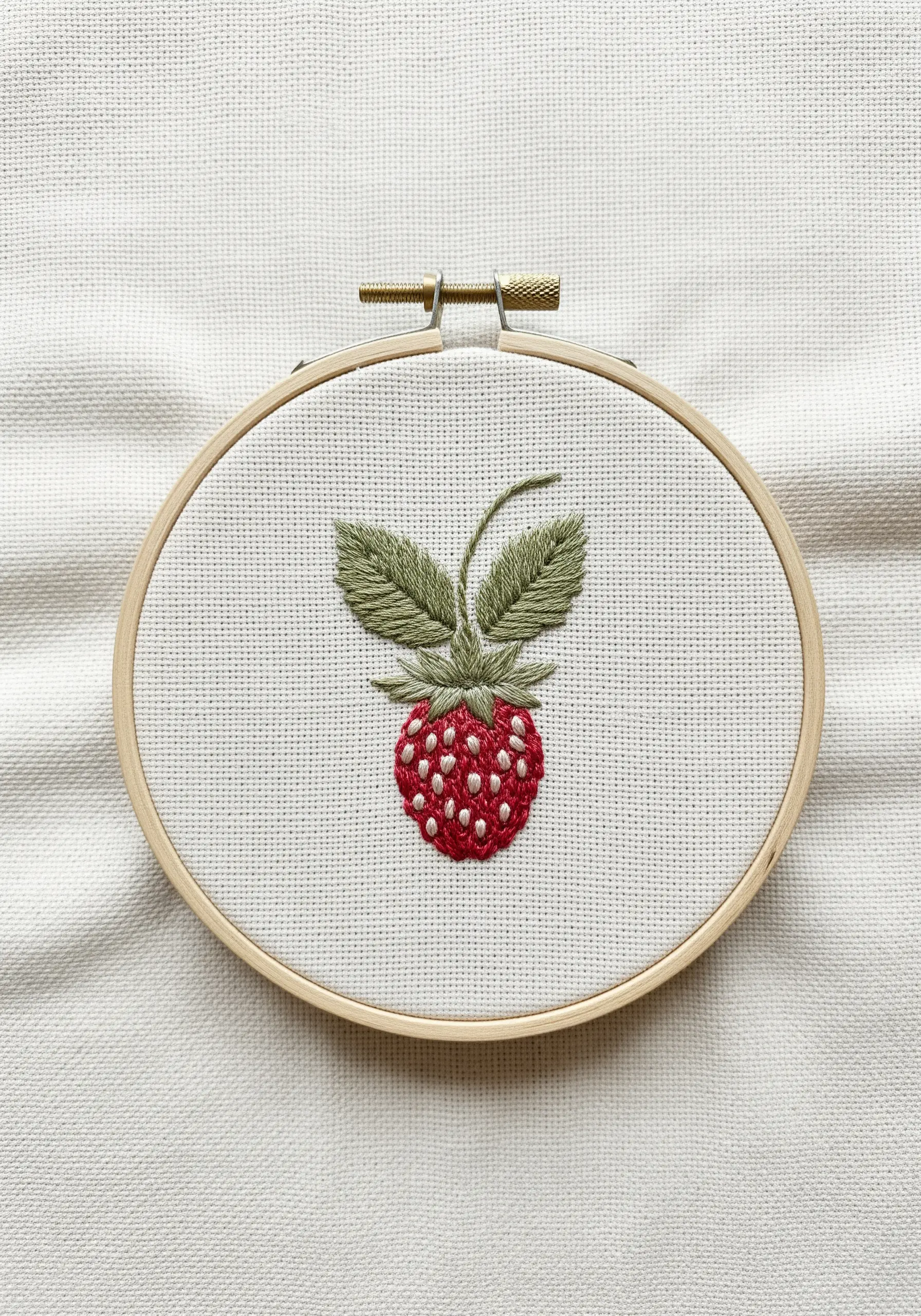 Embroidered strawberry with red satin stitch and white seed stitches.