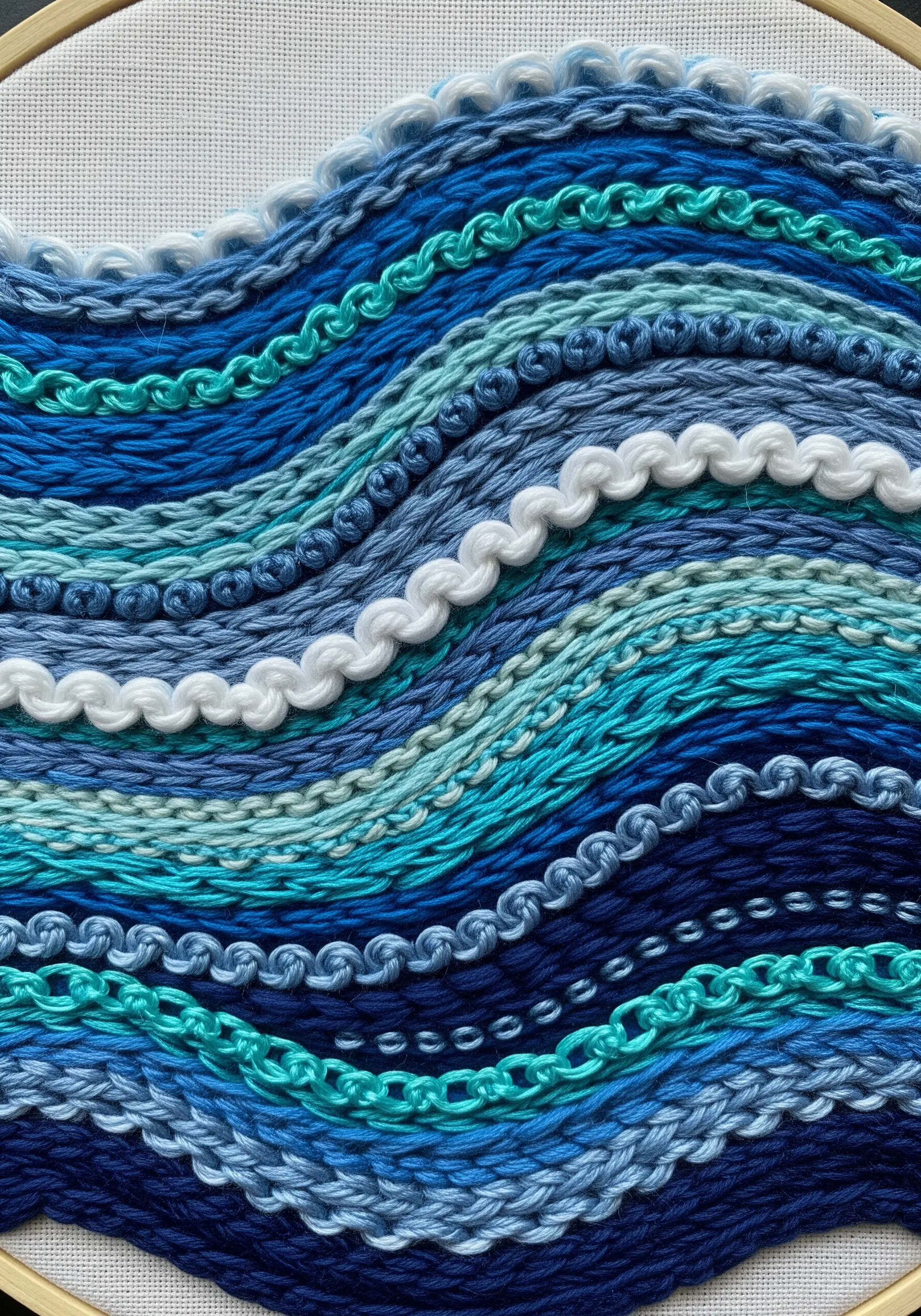 Close-up of abstract embroidered waves using various blue and white textural stitches.