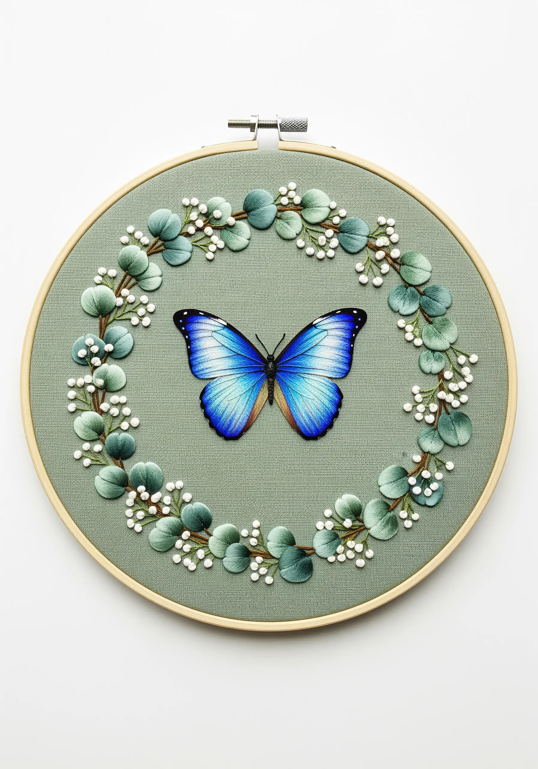 A Blue Morpho butterfly centered in a wreath of padded satin stitch eucalyptus leaves.