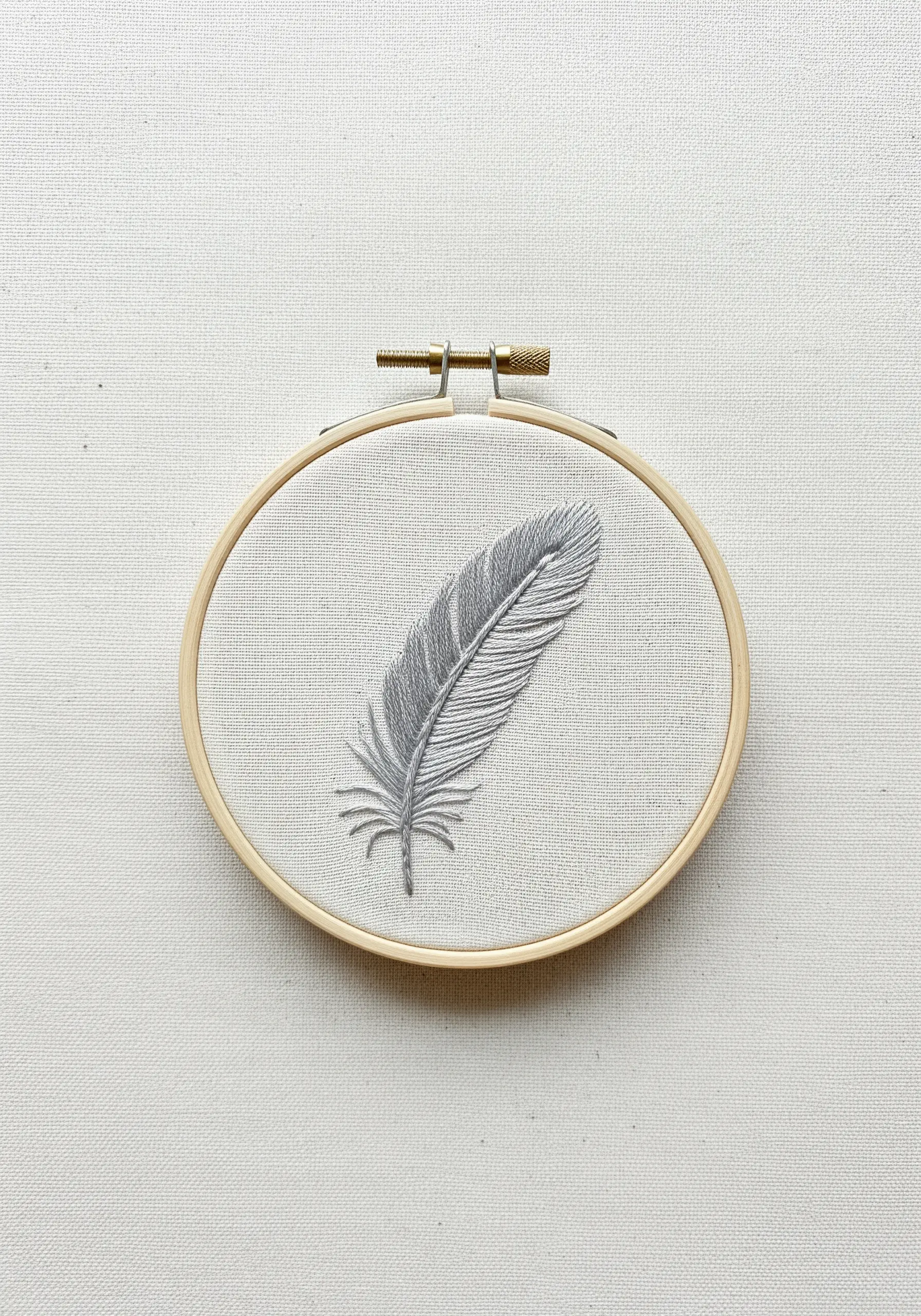 A delicately embroidered gray feather with stitches angled to show texture.