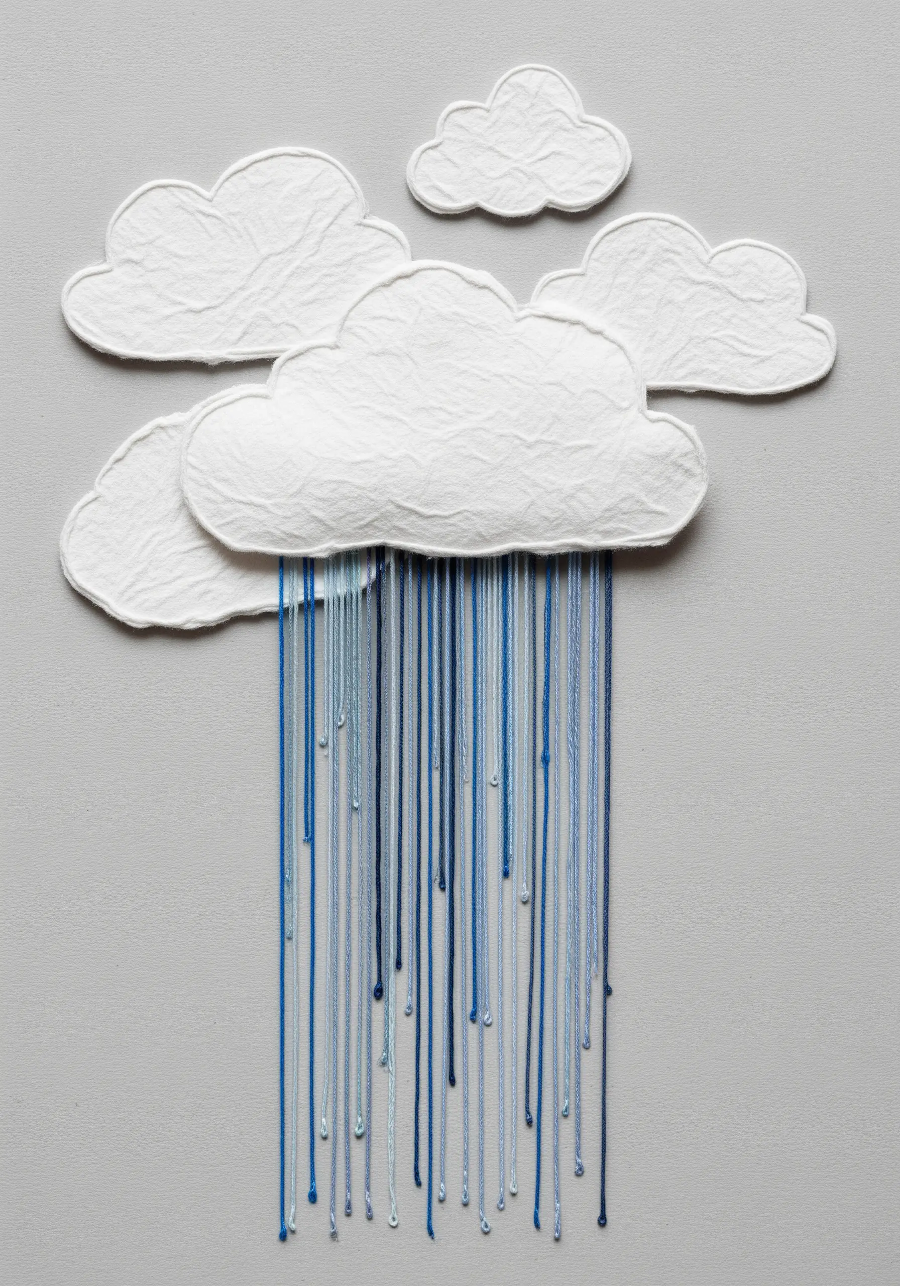 Textured white paper clouds with variegated blue threads hanging down to represent rain.