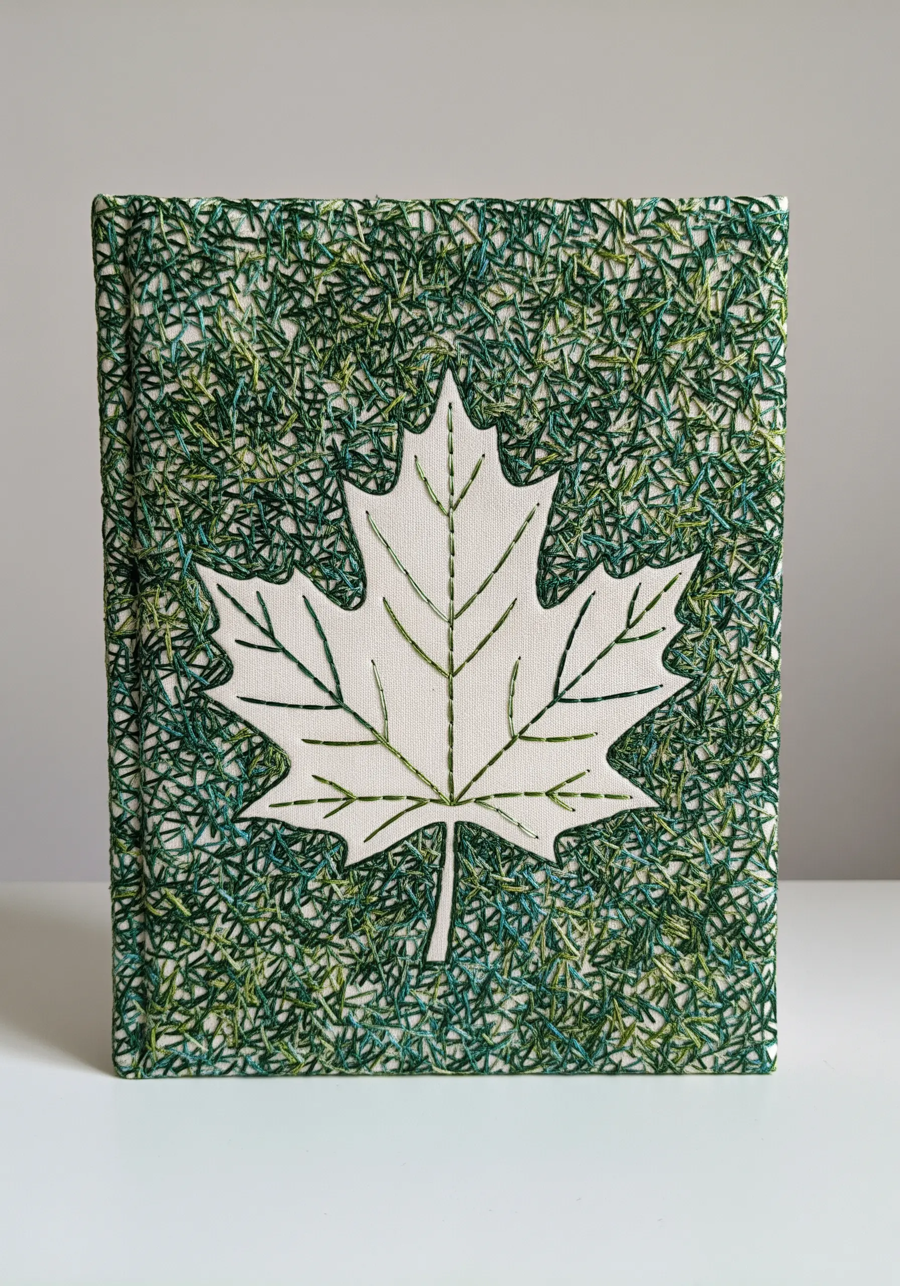 A white maple leaf shape created by filling the background with dense green stitches.