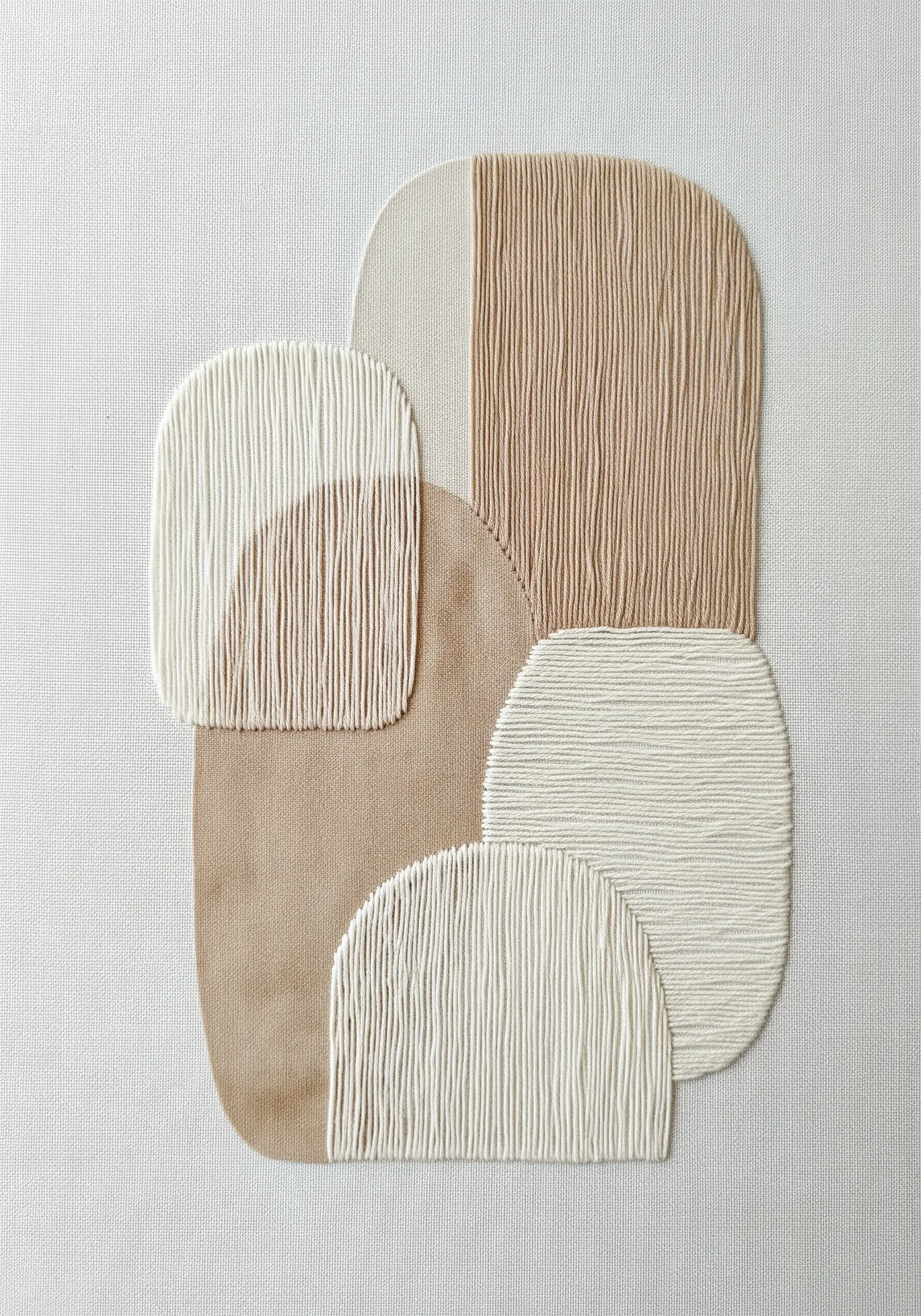 Abstract collage of layered fabric shapes completely covered with vertical straight stitches.