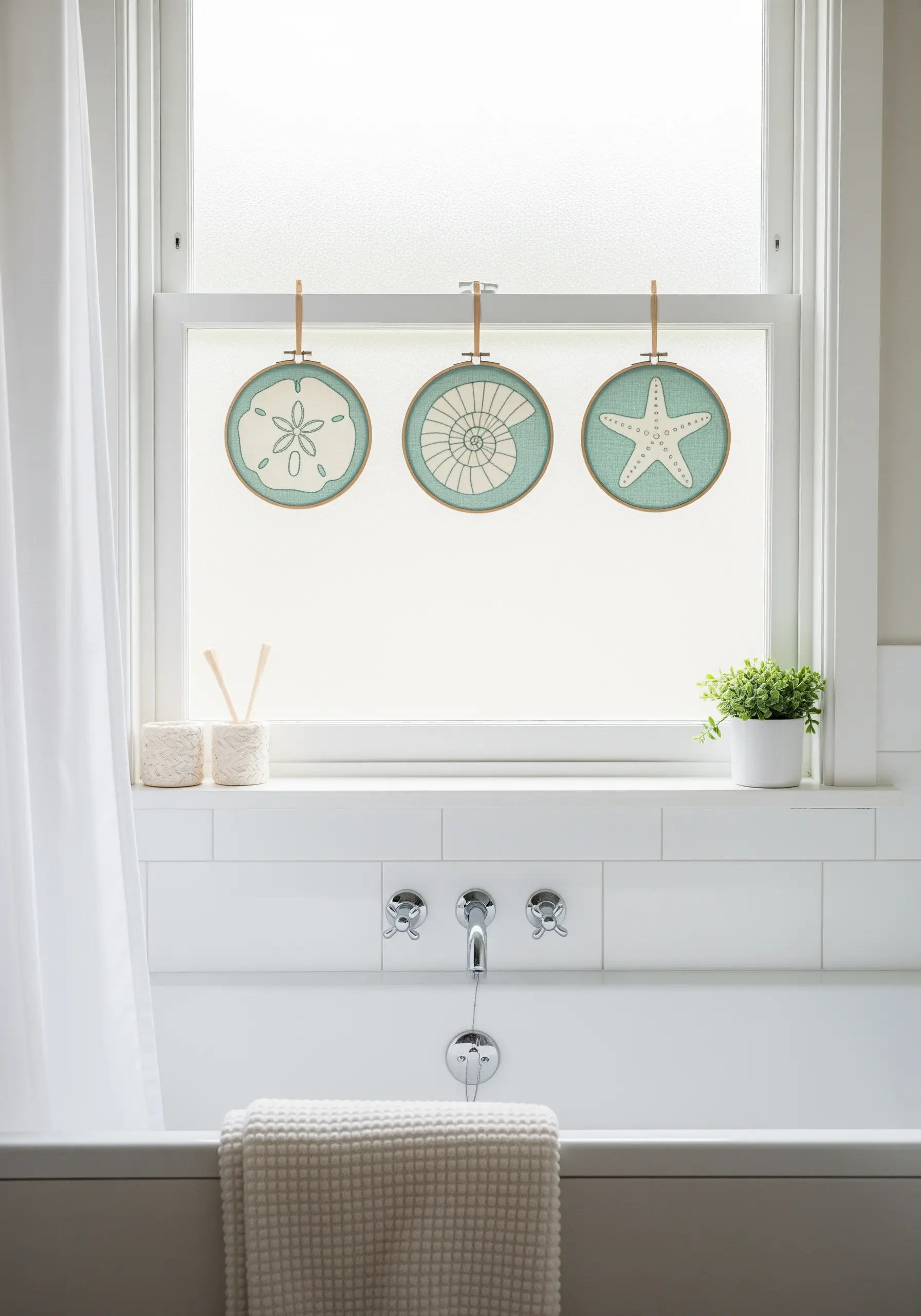 Three small embroidery hoops with seashell and starfish motifs hanging in a window.