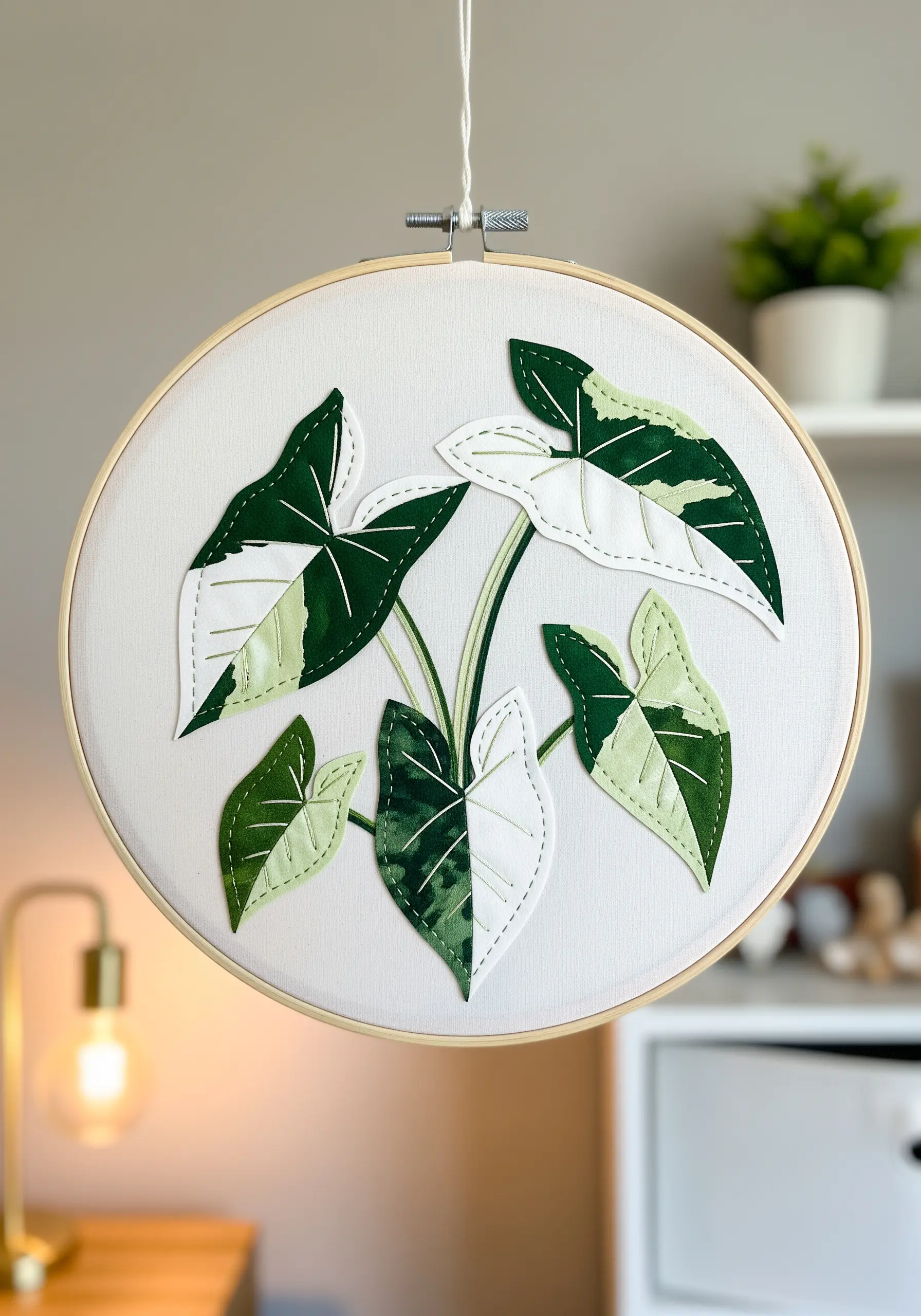 A hoop art piece depicting variegated Alocasia leaves made from fabric collage and simple embroidery.