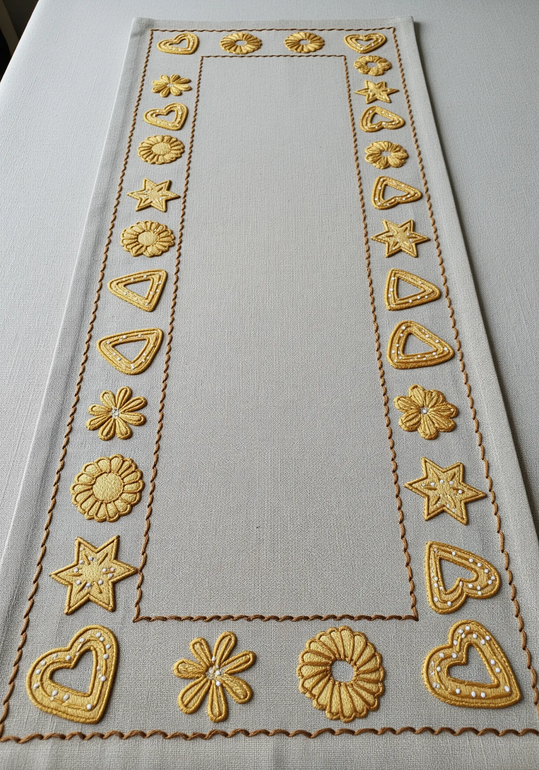 A table runner border embroidered with various golden satin-stitched cookie shapes.