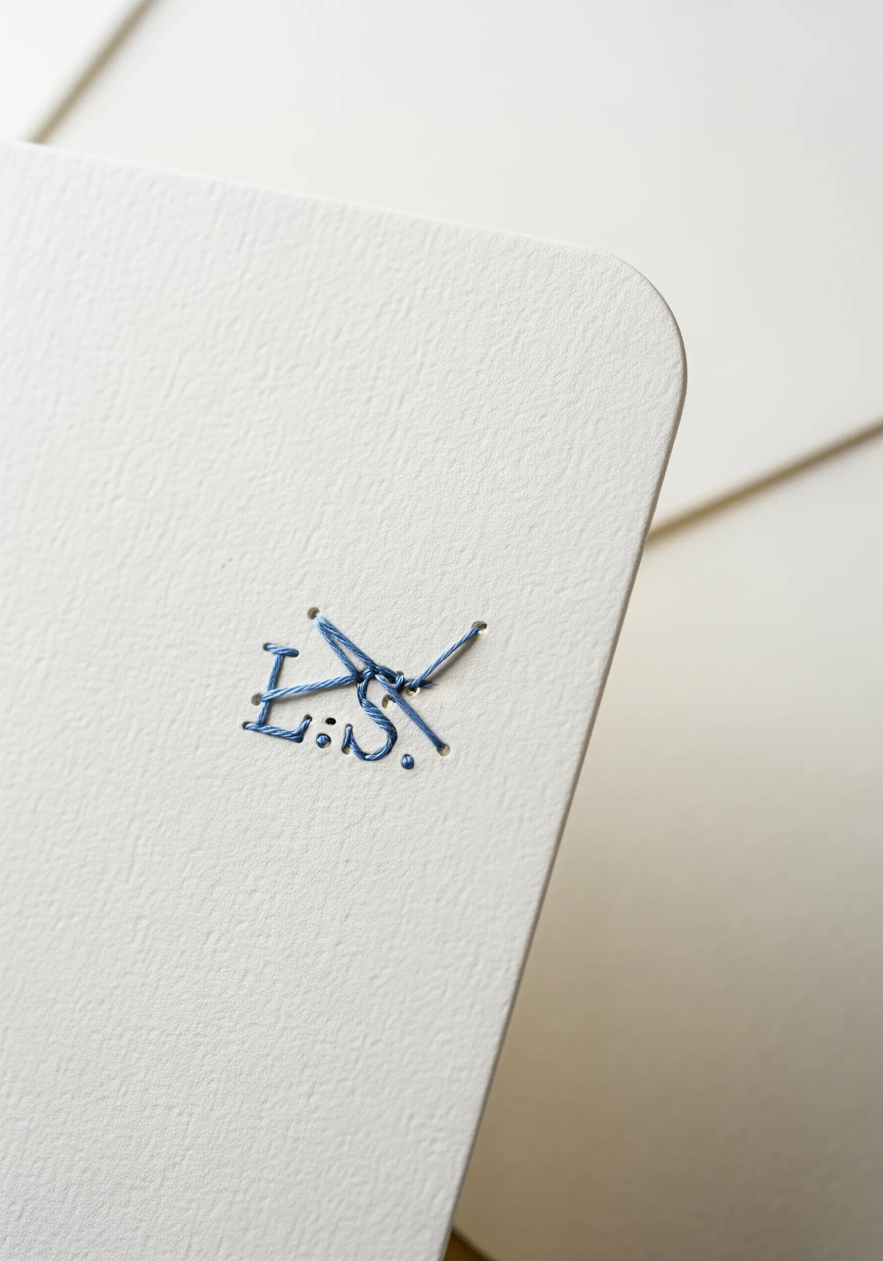 Abstract initials 'L.S.' stitched in blue thread onto textured white cardstock.