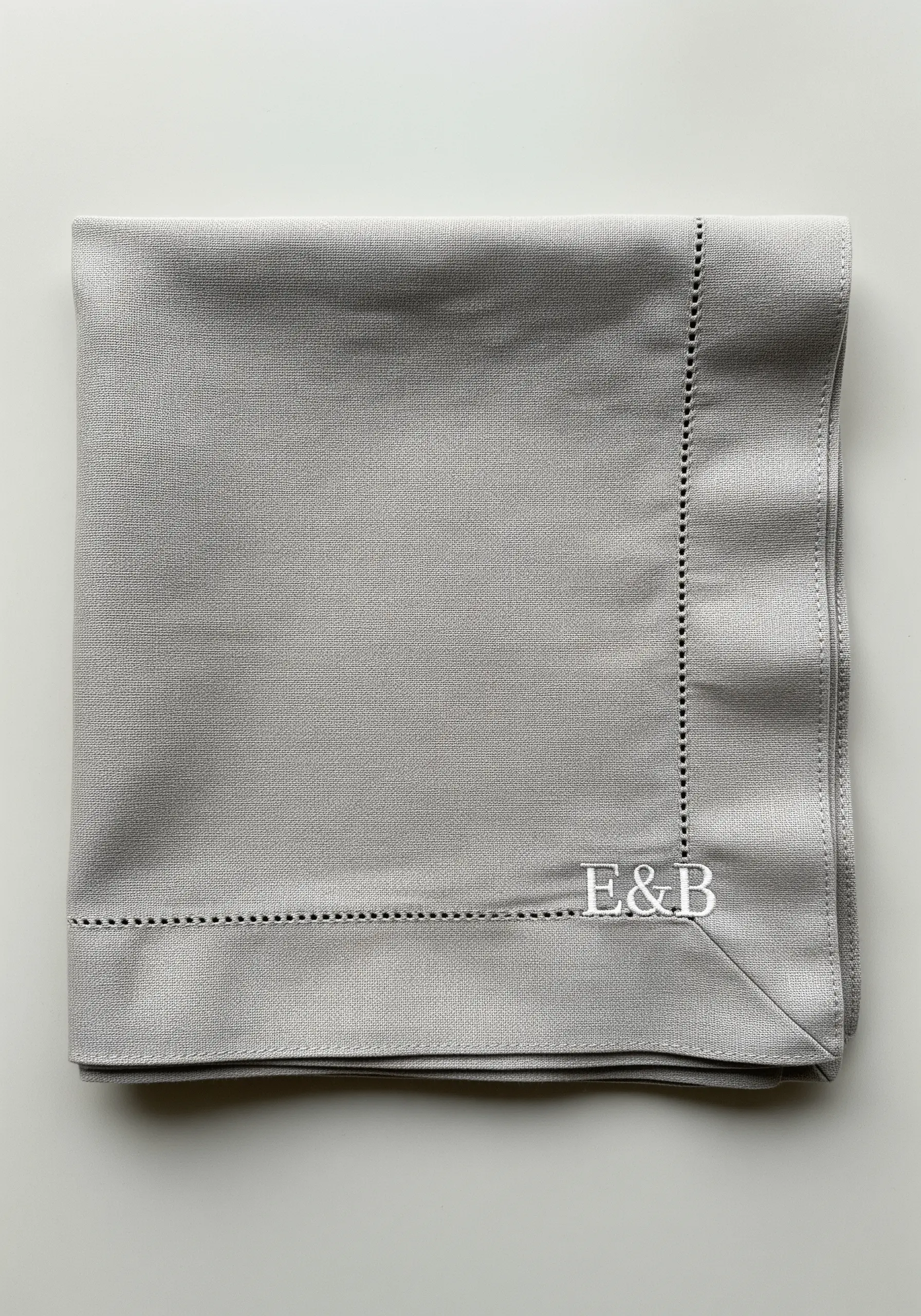 Elegant raised white satin stitch monogram 'E&B' on a grey linen napkin.