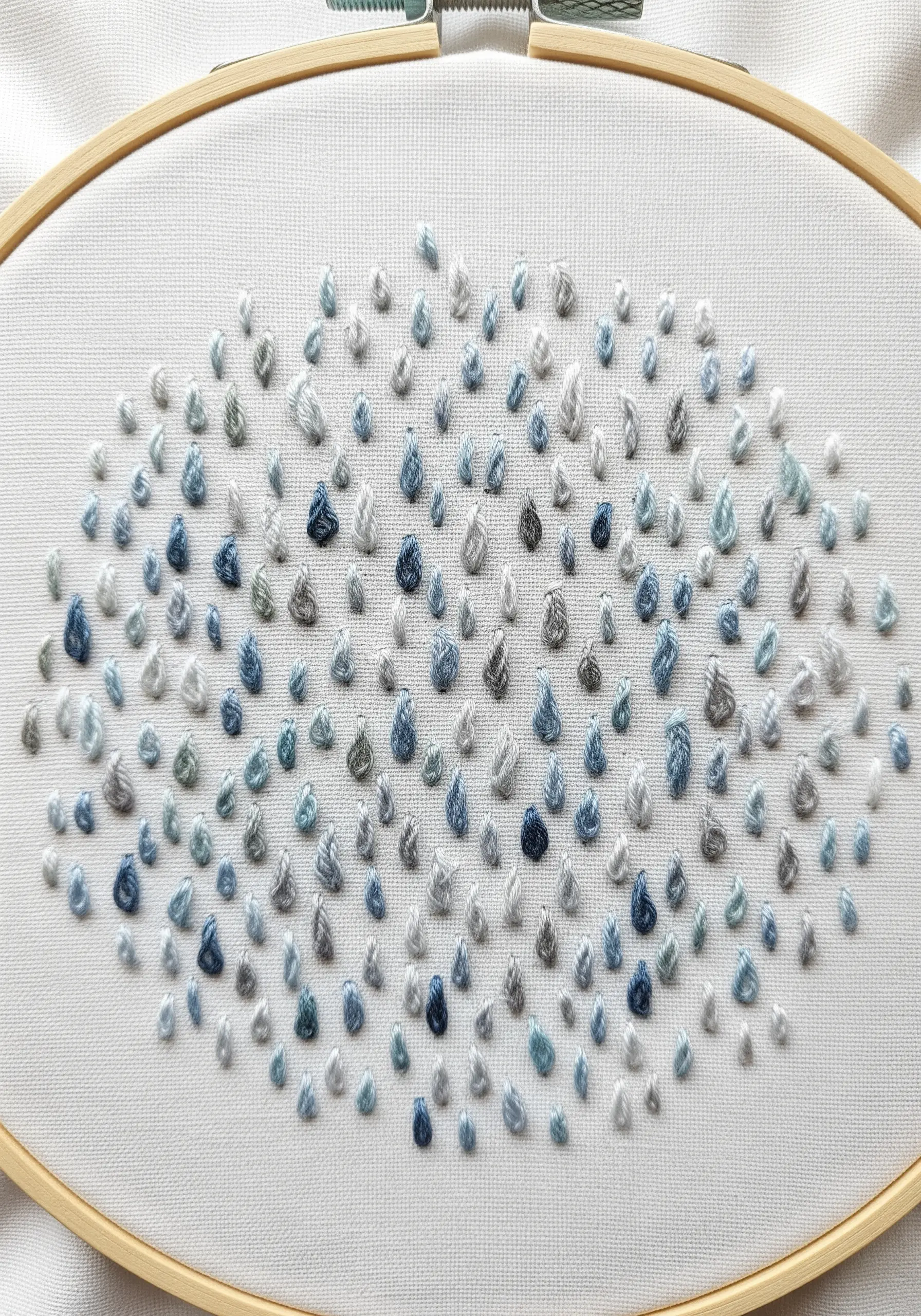A collection of scattered French knots in various shades of blue, gray, and white.