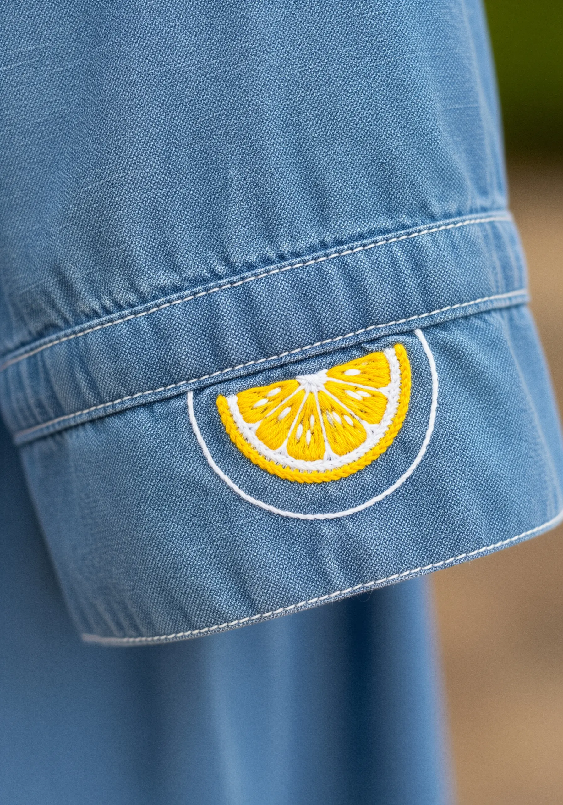 Embroidered lemon slice on a denim shirt cuff with detailed satin stitch segments.