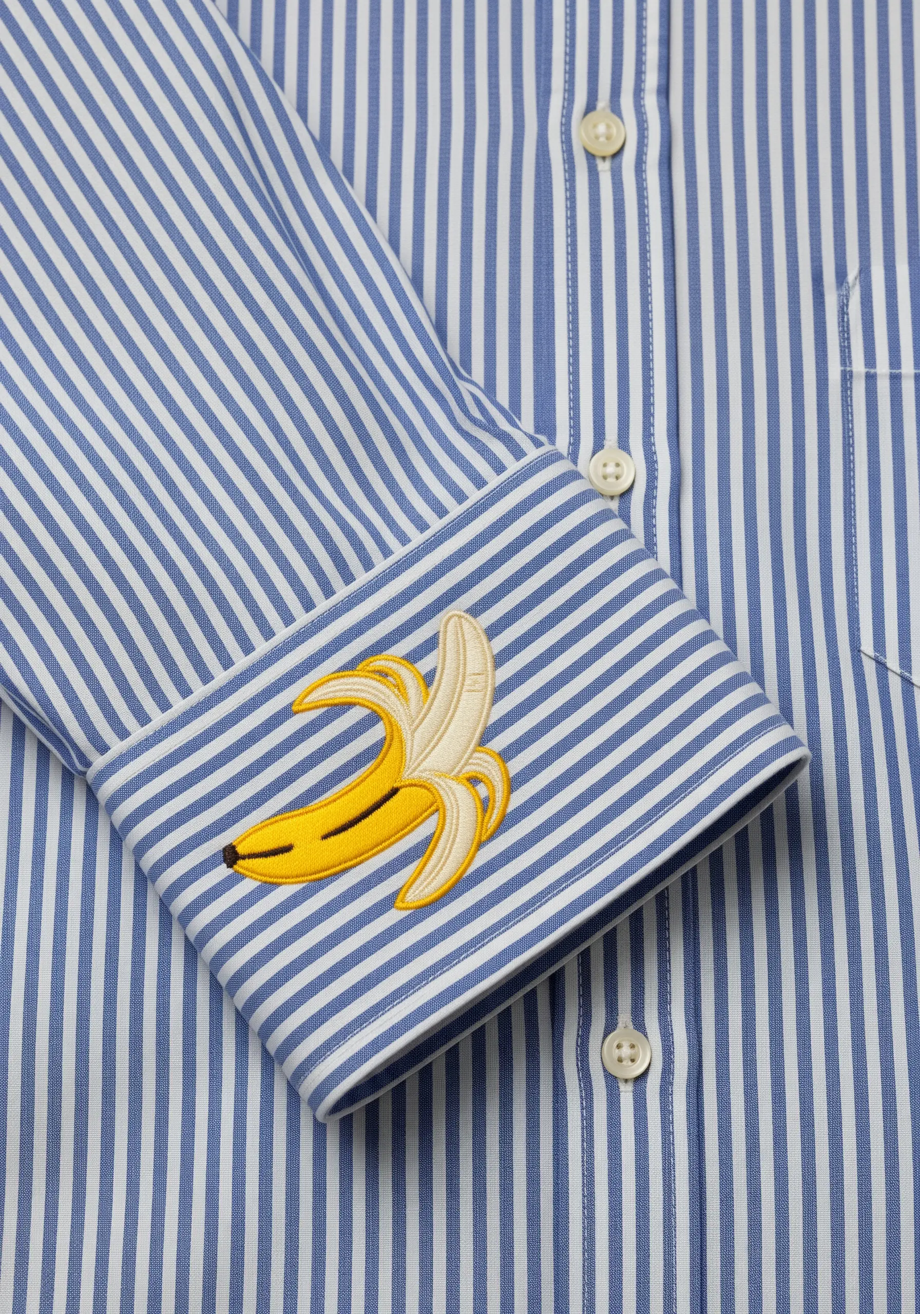An embroidered peeled banana on the cuff of a blue and white striped shirt.