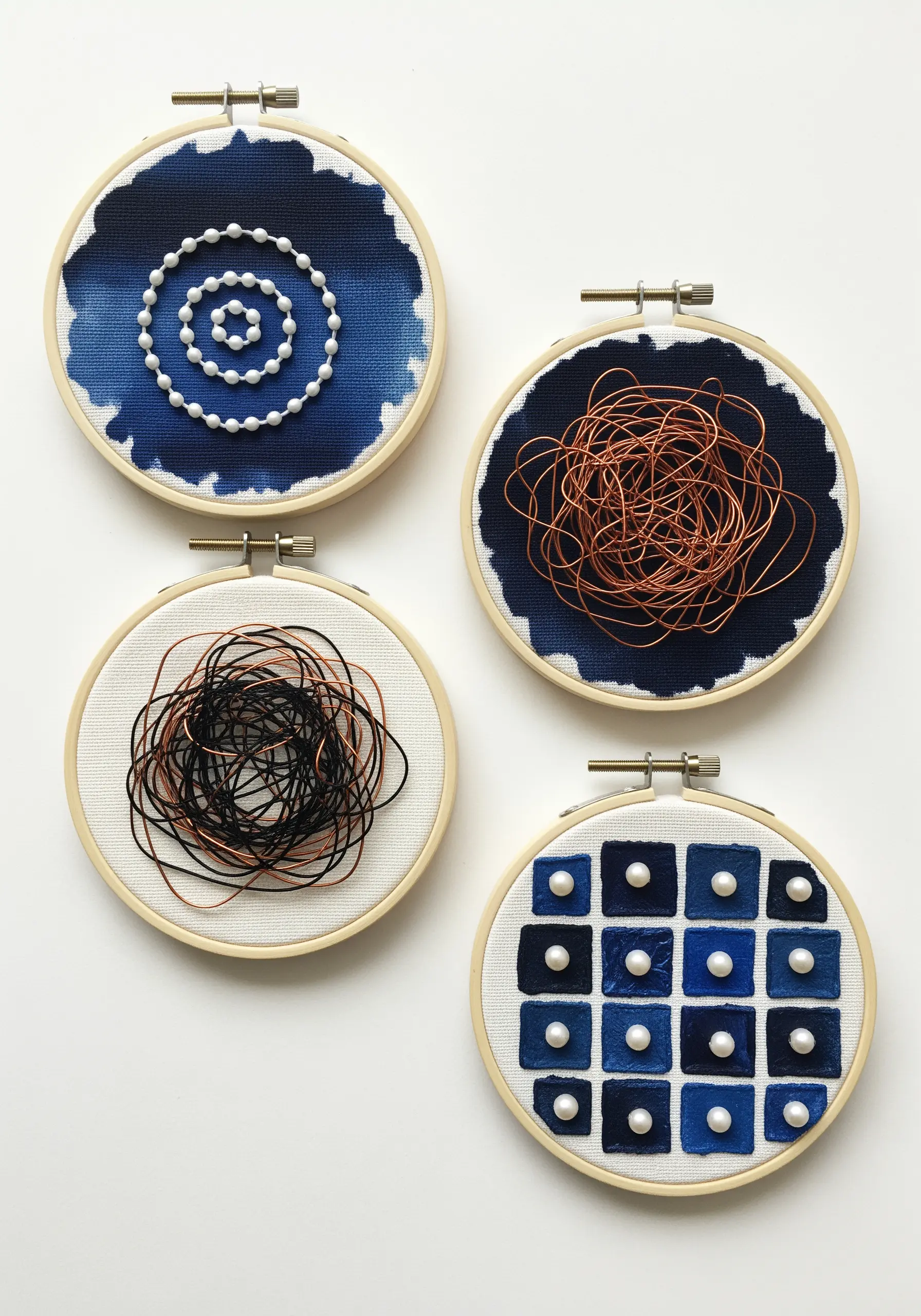 Four small embroidery hoops with abstract designs using indigo dye, beads, and copper wire.
