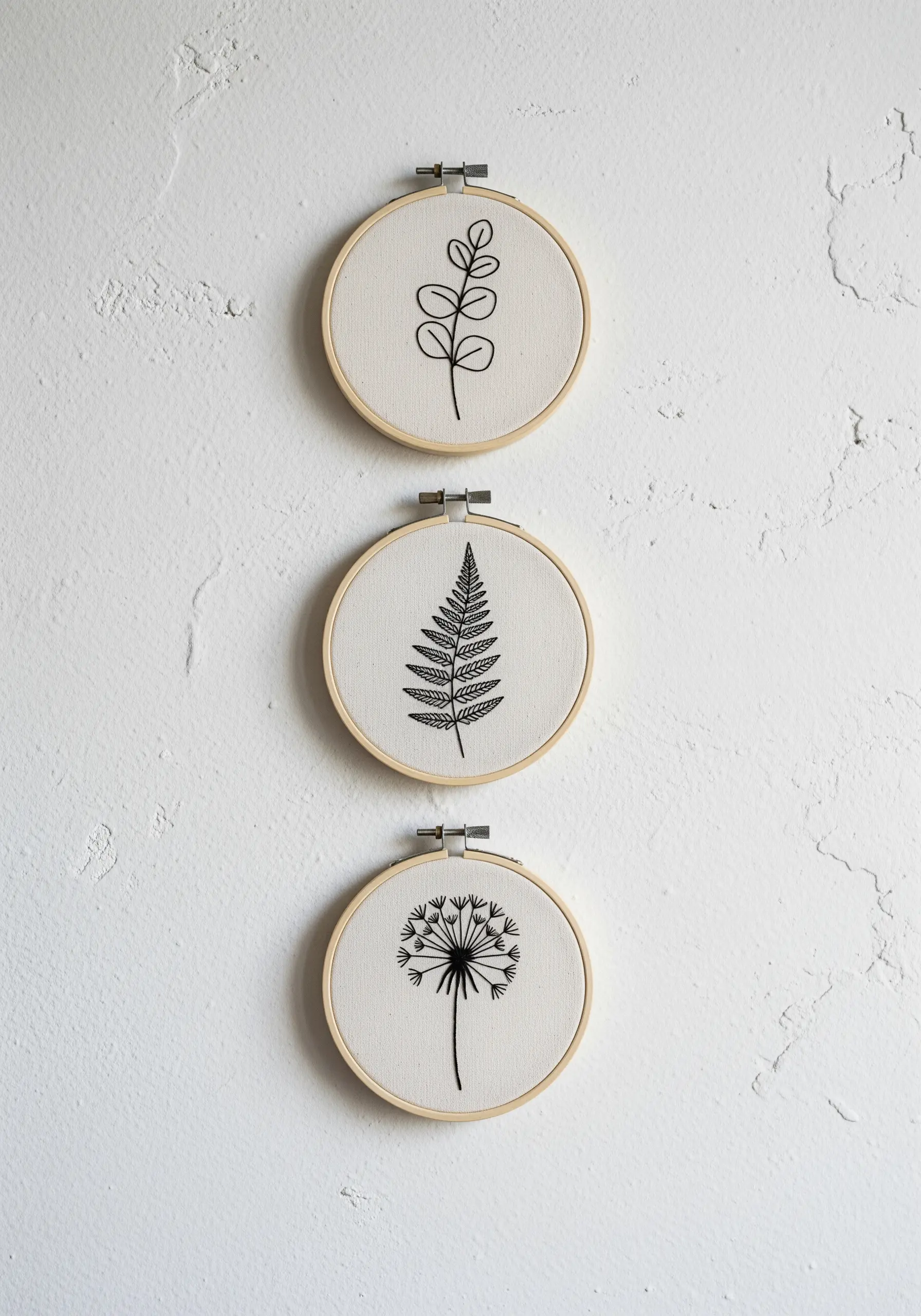 A triptych of embroidery hoops with minimalist black line art of different botanicals.