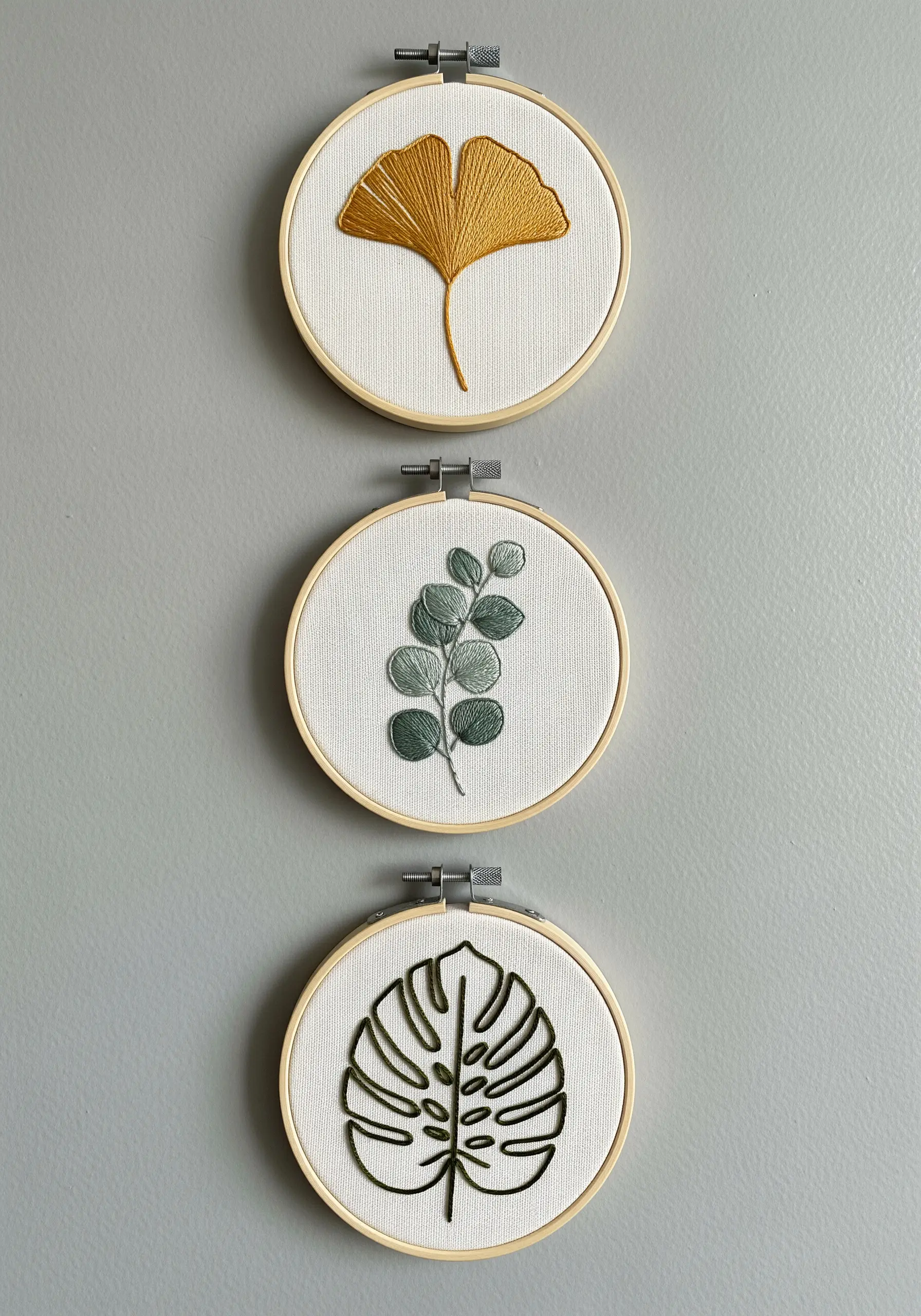 A trio of small embroidery hoops, each featuring a different minimalist leaf design.