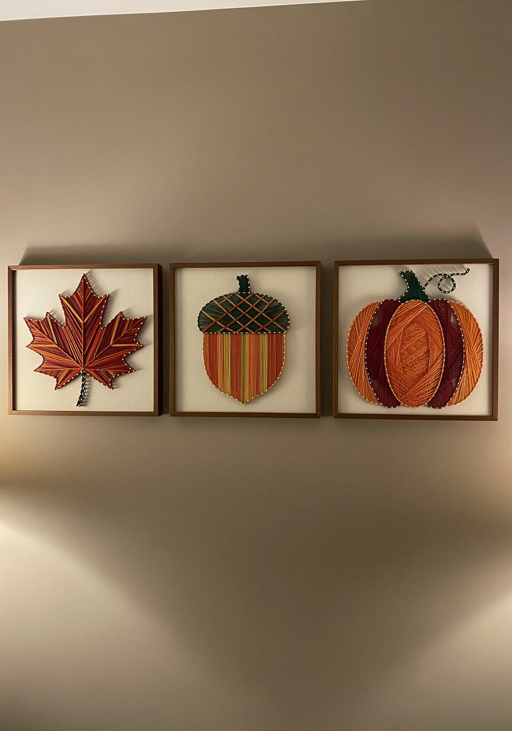 Triptych of fall-themed string art: a maple leaf, an acorn, and a pumpkin.