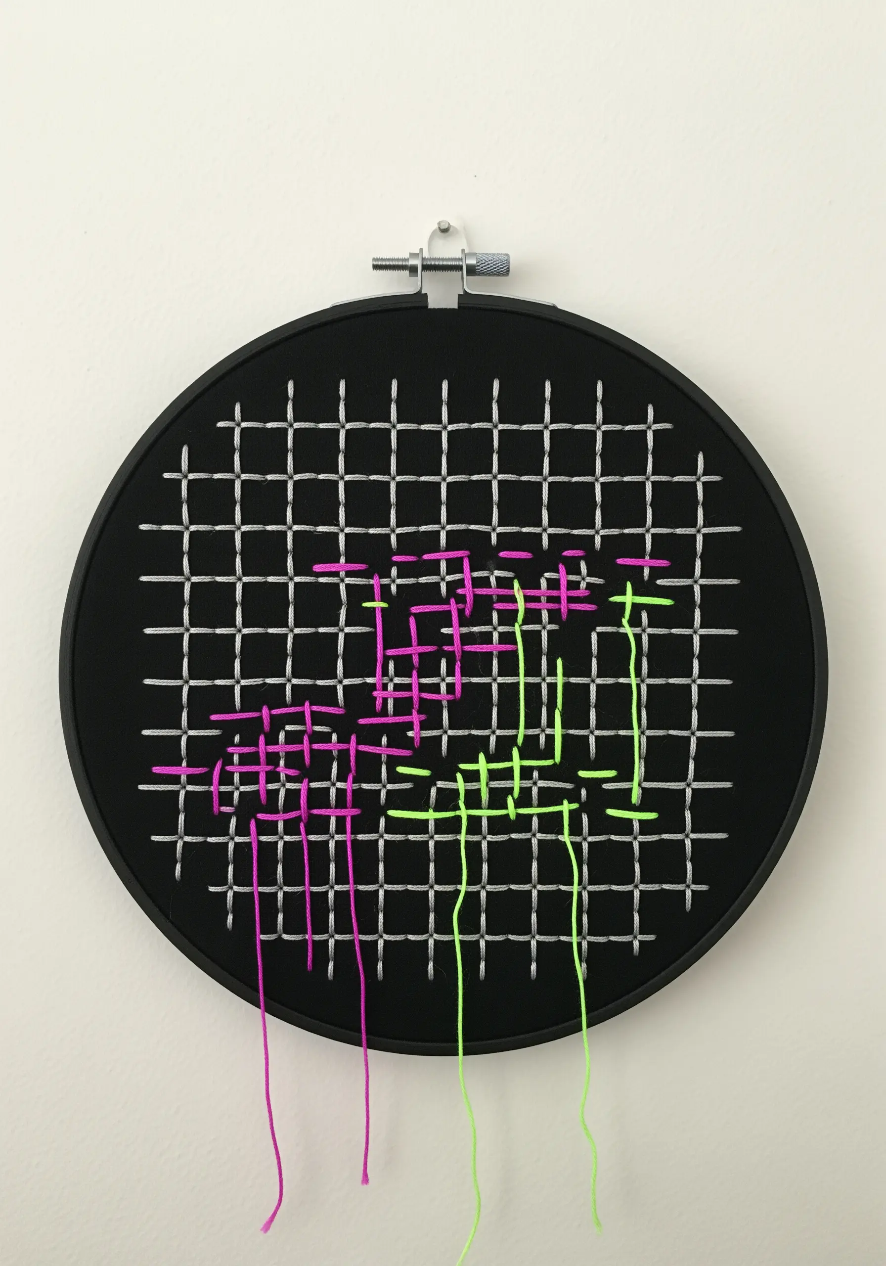 A woven grid of silver thread on black fabric, with neon pink and green thread woven through.