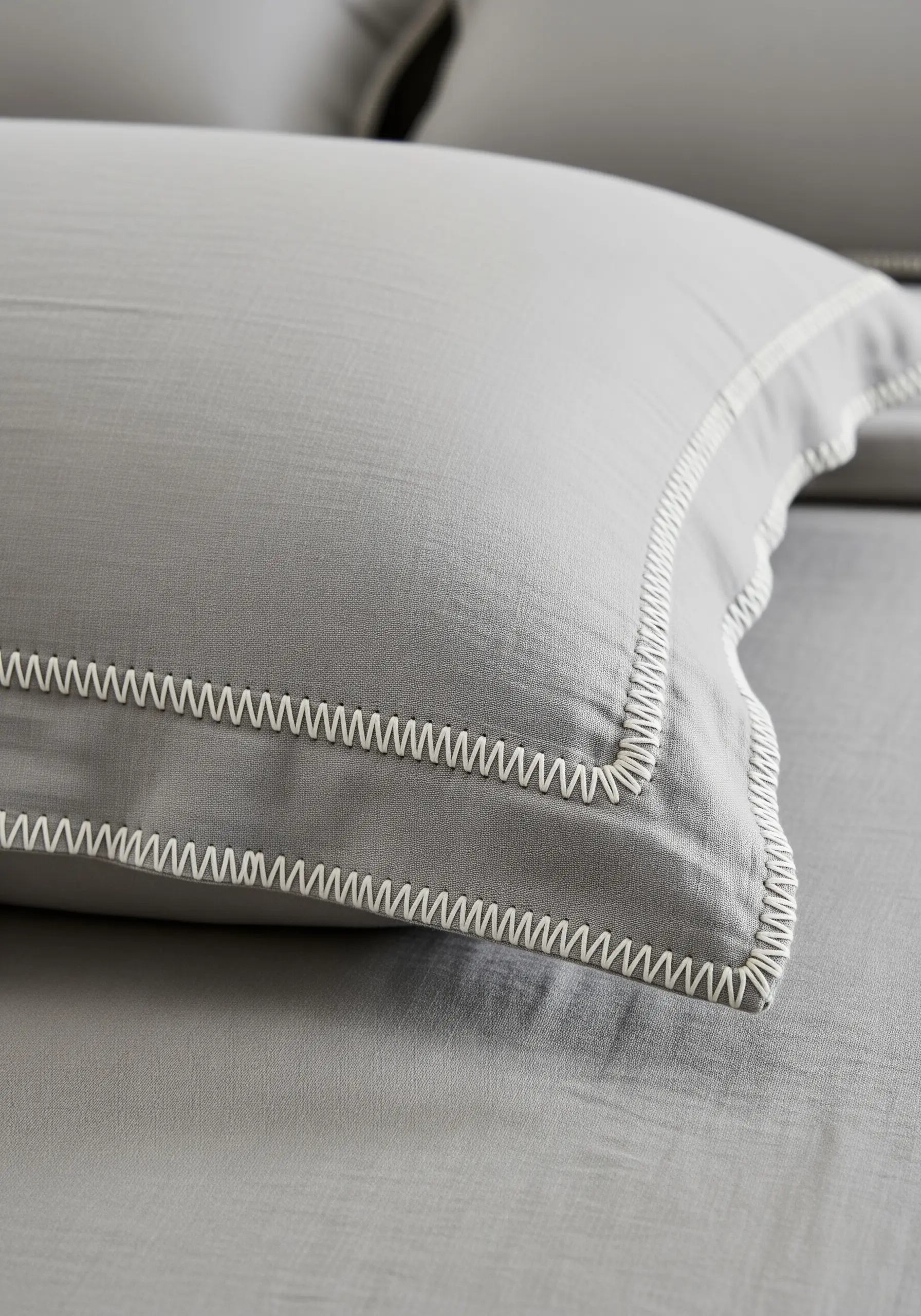 A close-up of a gray pillowcase with a crisp, white blanket stitch embroidered along the edges.