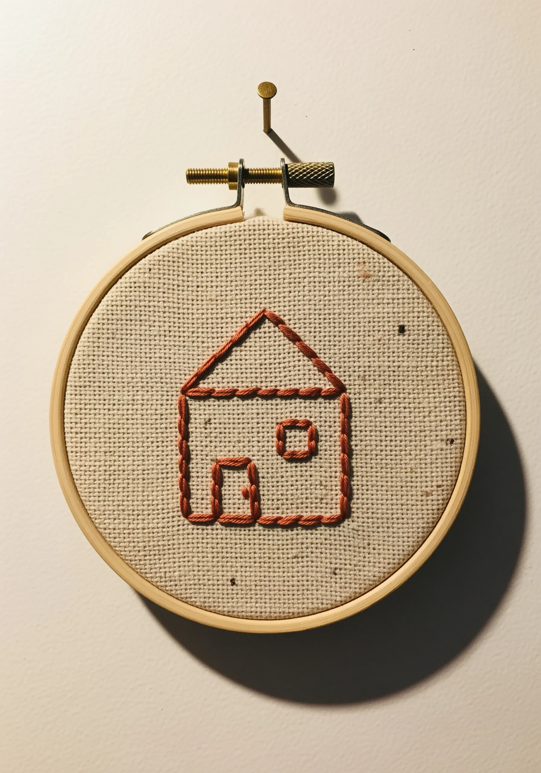 A simple house shape embroidered with a thick, textured outline stitch in terracotta thread.