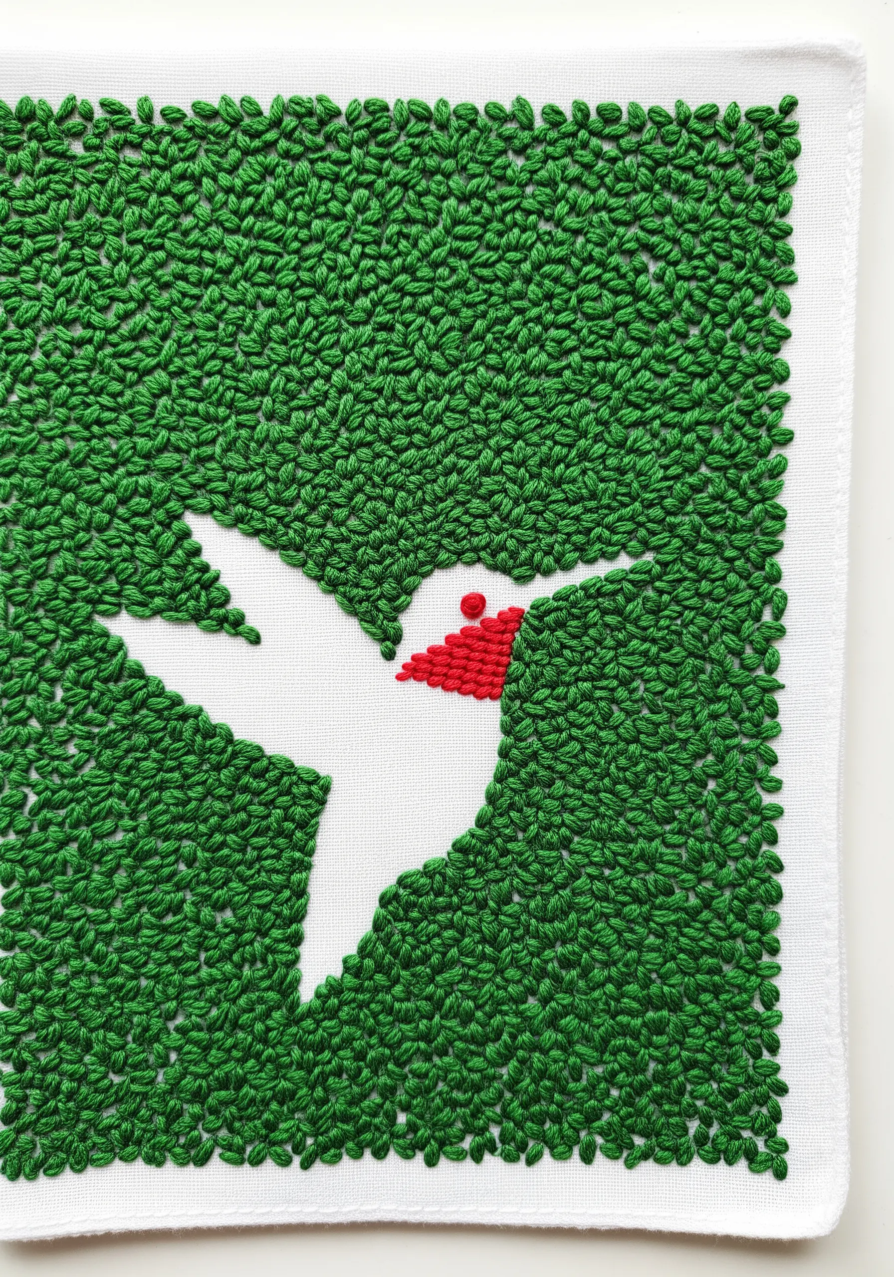 A white hummingbird silhouette created by filling the background with green stitches.