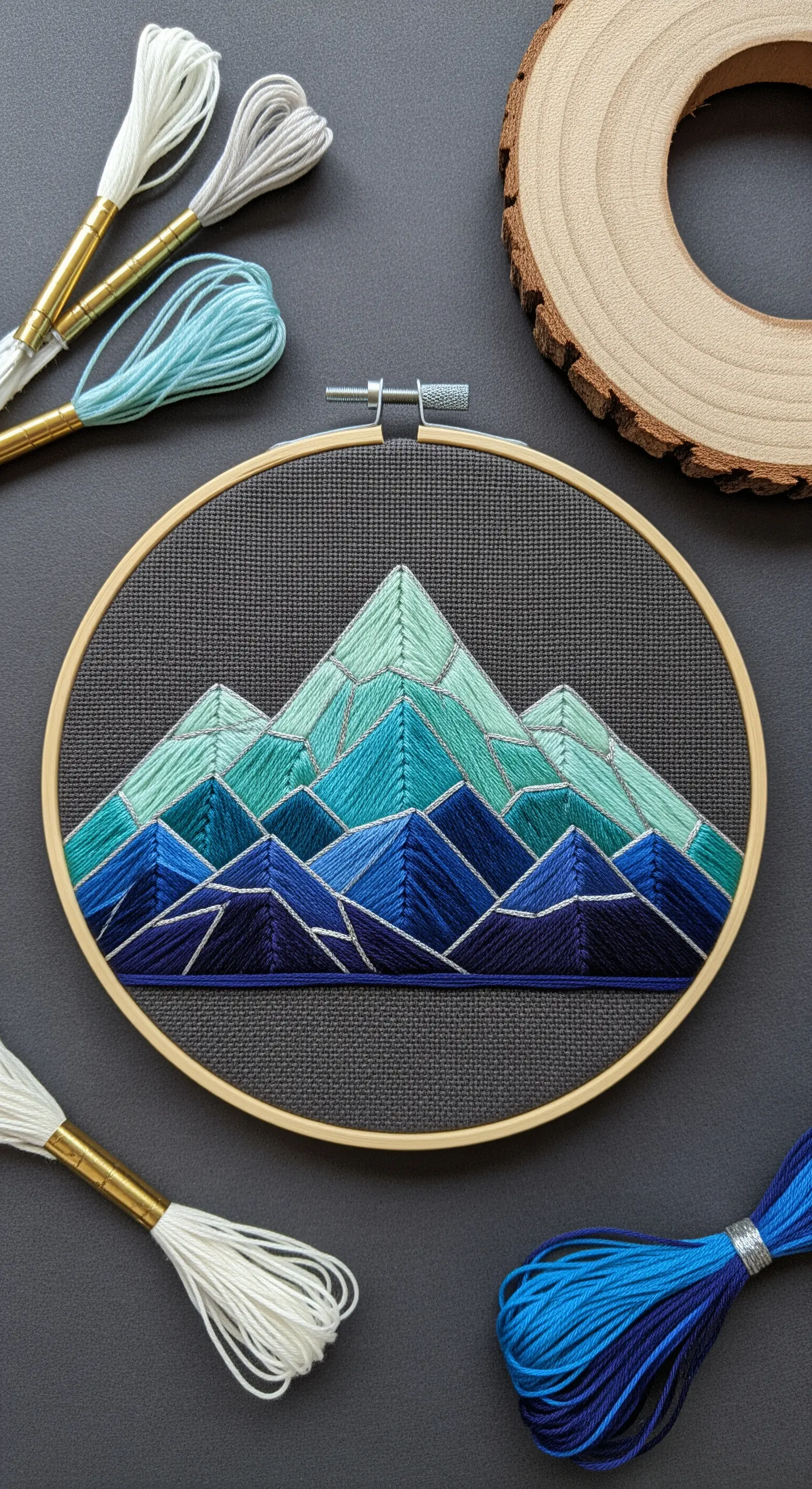Geometric mountain embroidery with blue and green satin stitch on dark gray fabric.
