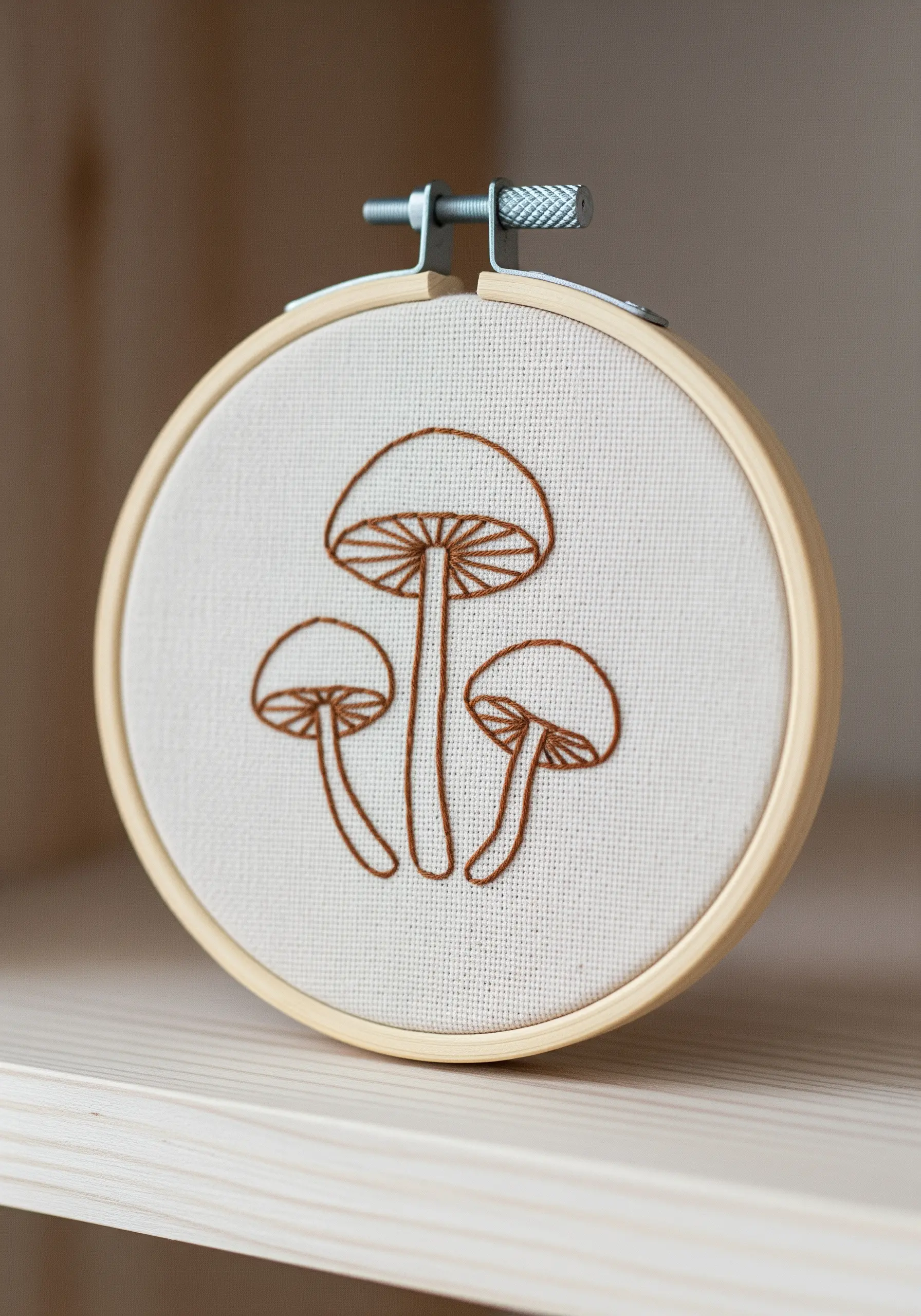 Three mushrooms outlined in brown thread in a simple, illustrative style.