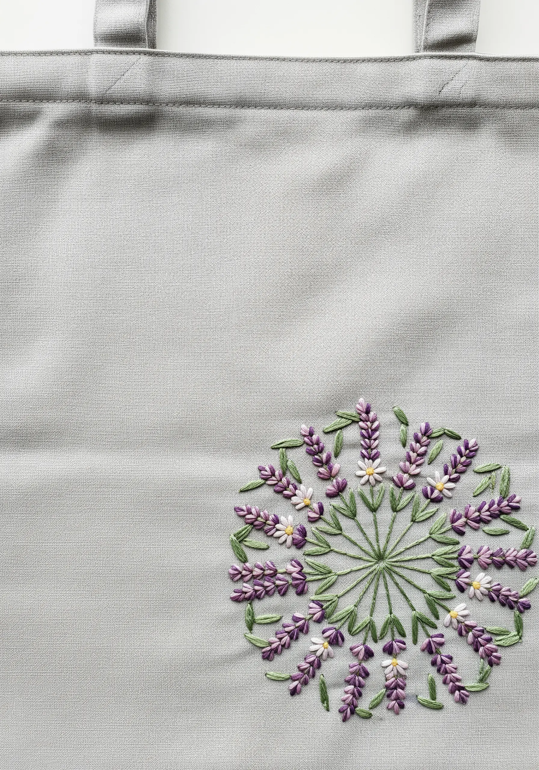 Delicate lavender and chamomile flowers embroidered in a circular pattern on a grey tote bag.