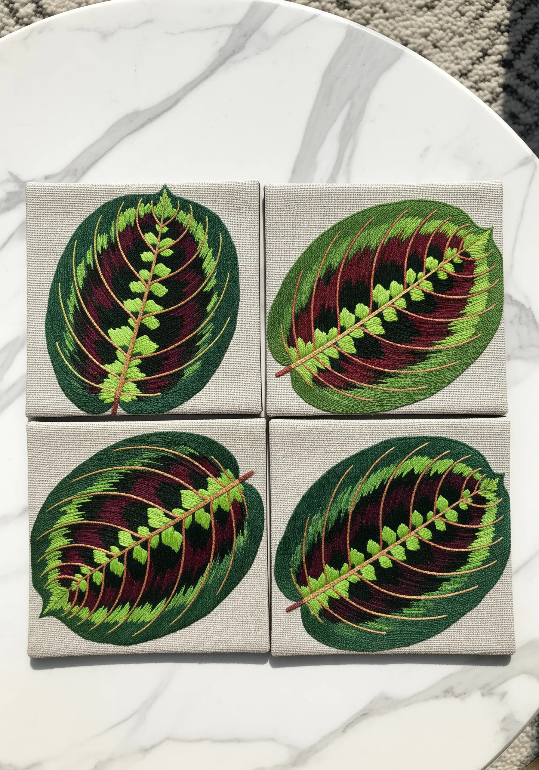 A set of four embroidered coasters, each featuring a detailed Maranta 'Prayer Plant' leaf.