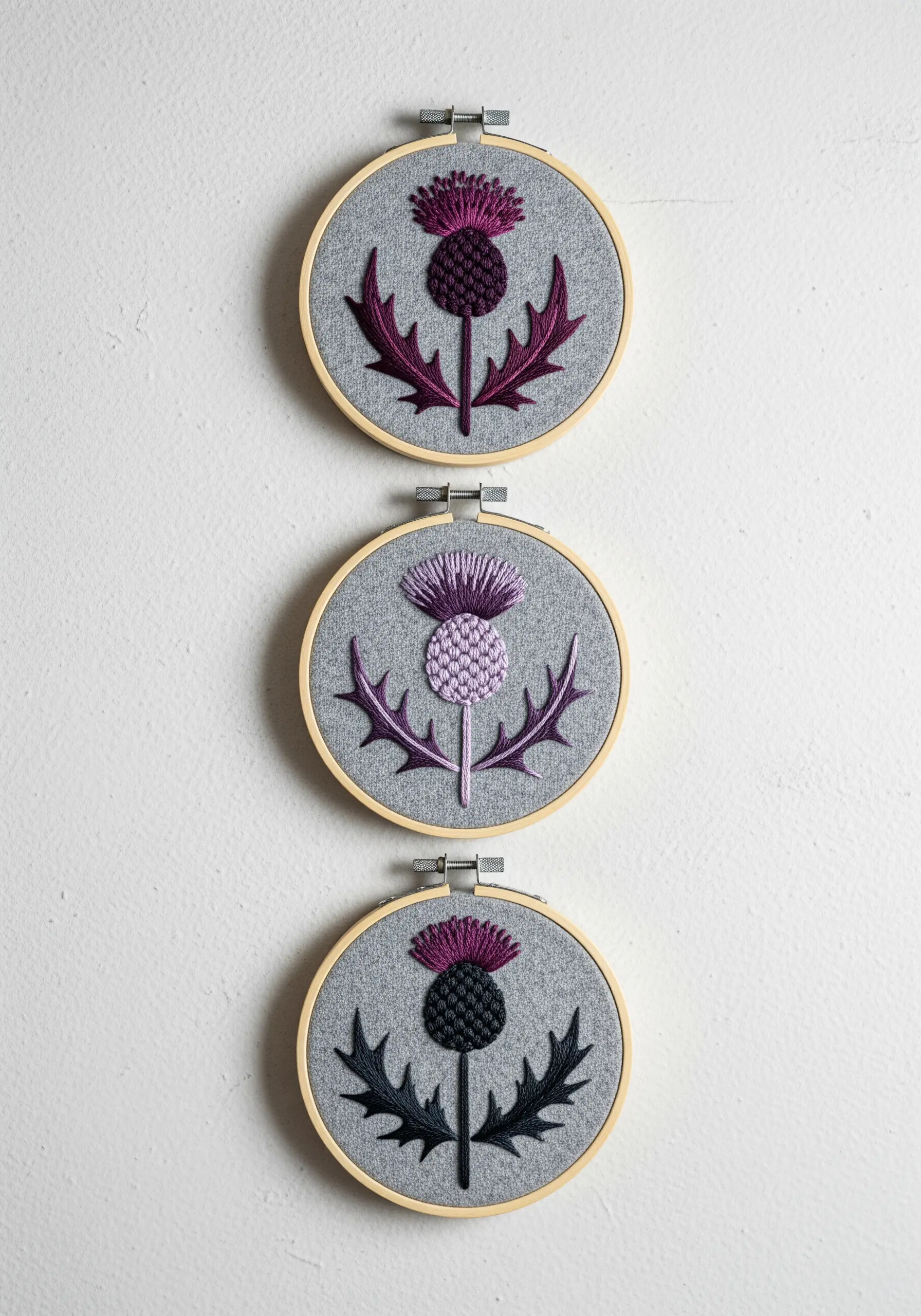 Three embroidery hoops showing the same thistle design in different color palettes.