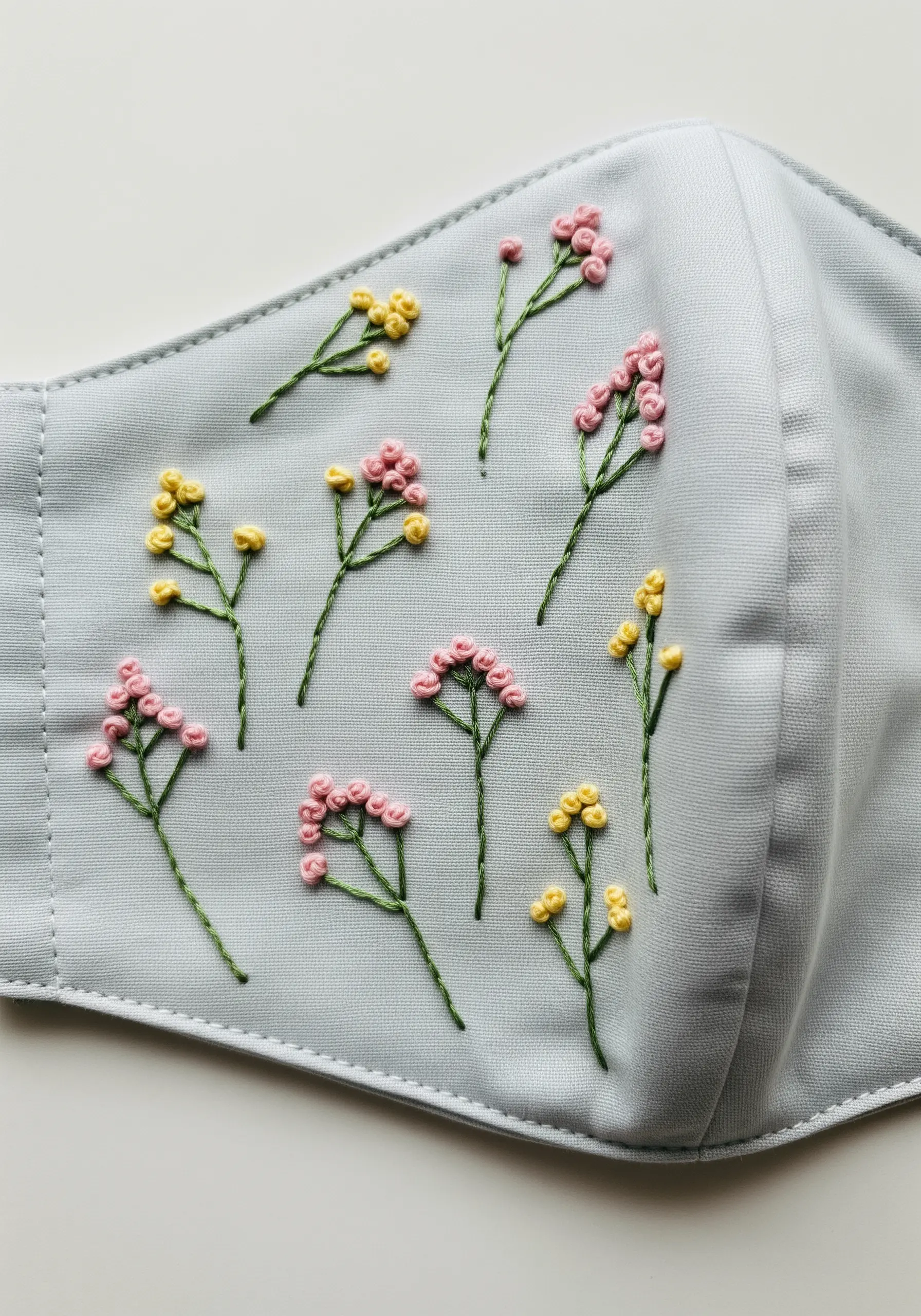 Scattered tiny flowers made with French knots on a light blue fabric face mask.