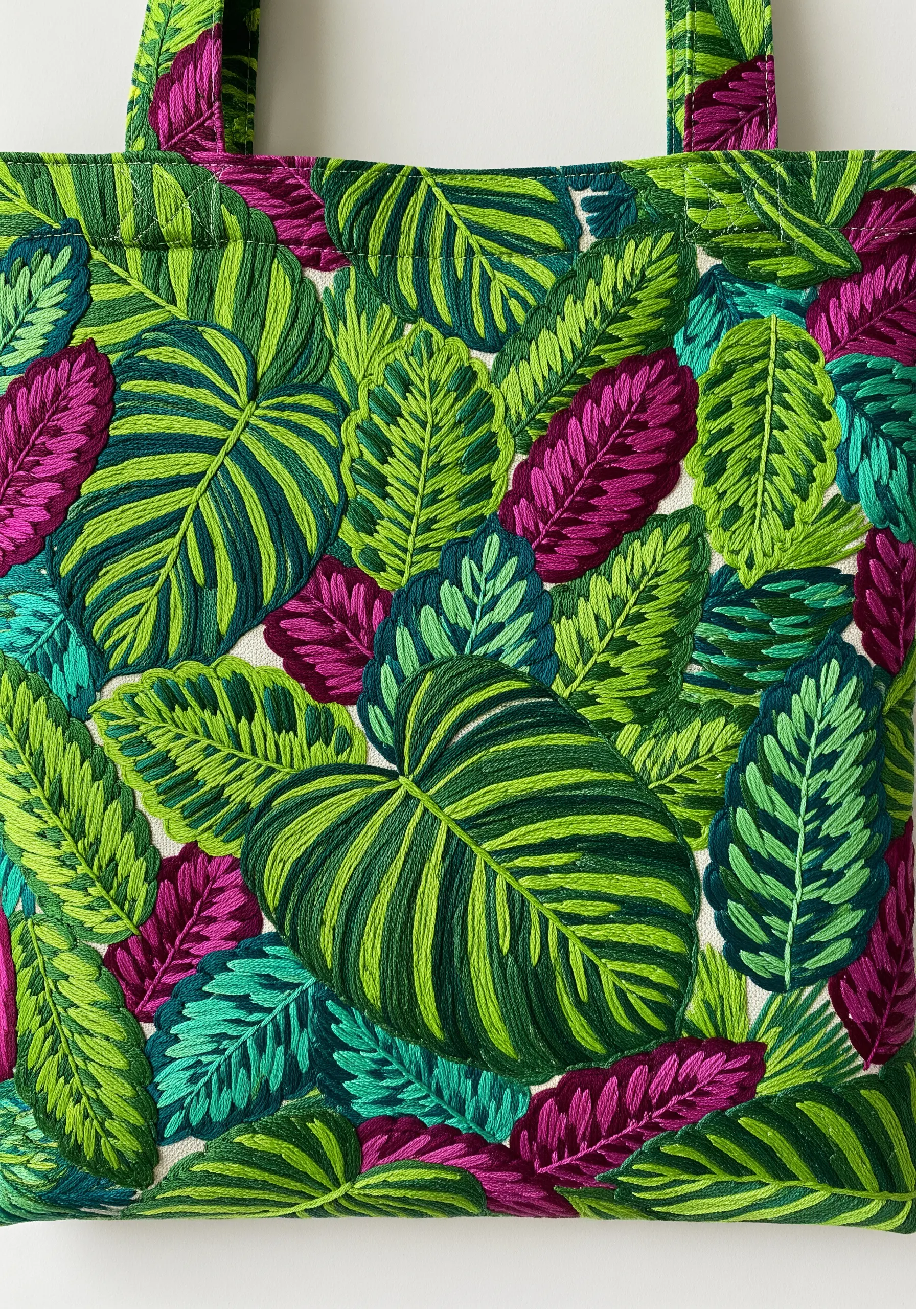 A densely embroidered tote bag covered in overlapping tropical leaves in green and magenta.