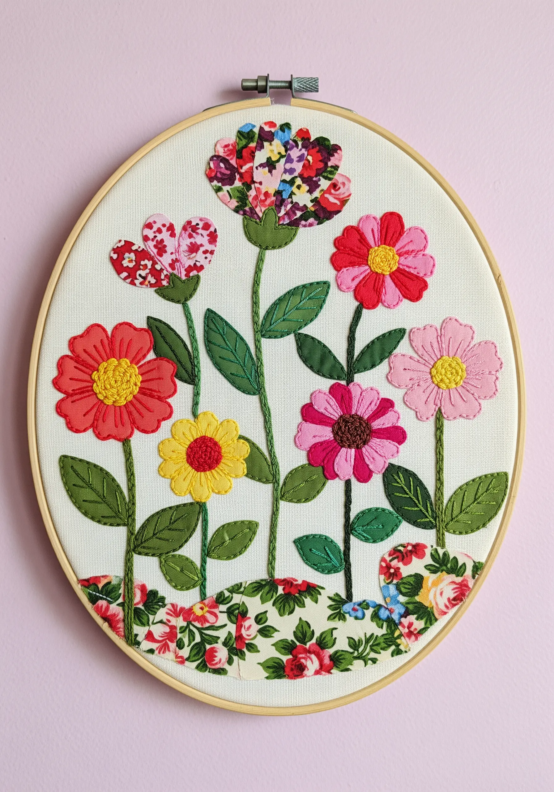 Floral hoop art with brightly patterned fabric appliqué flowers and embroidered stems.