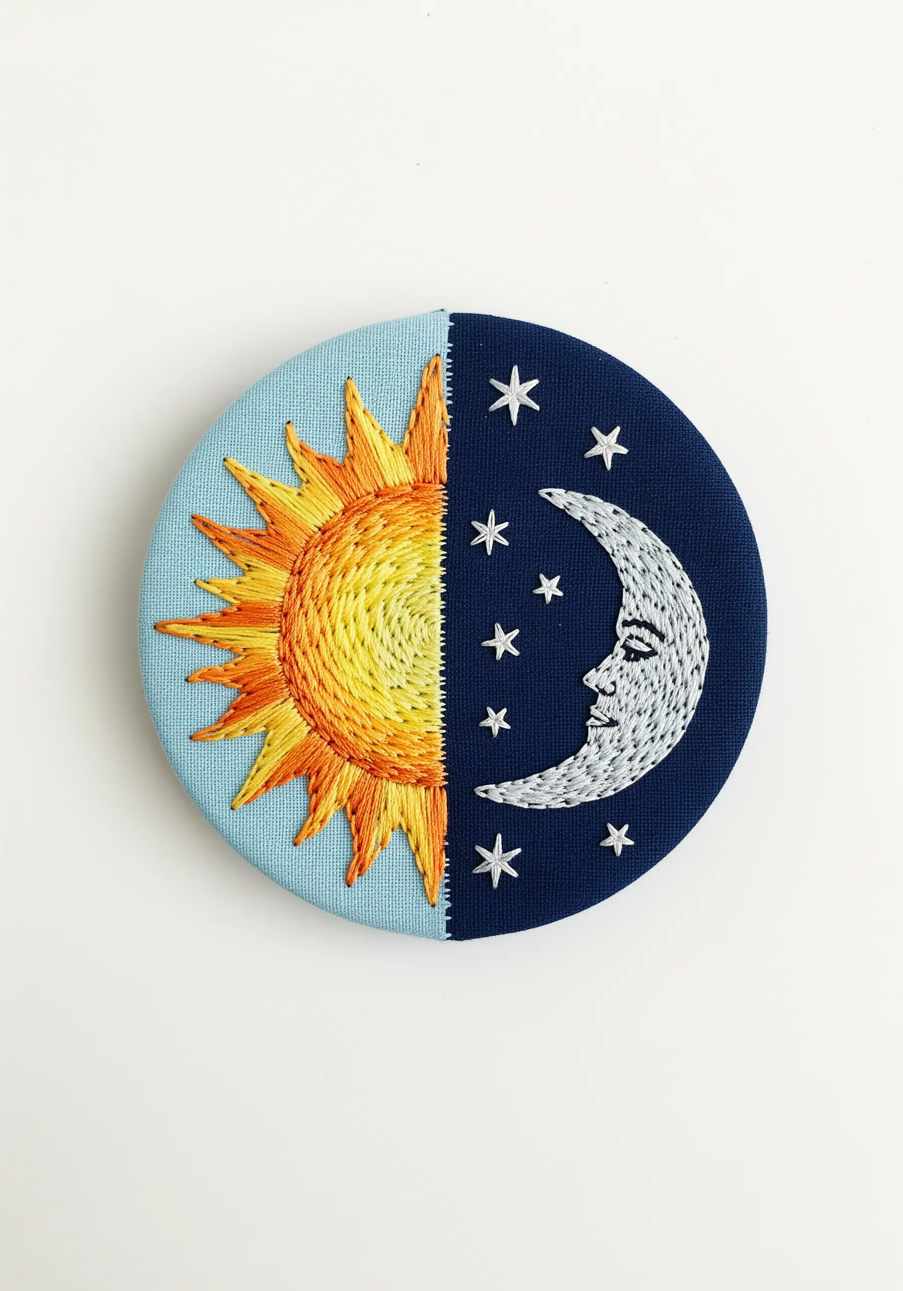 A circular embroidery split into a day and night scene with a sun and moon.