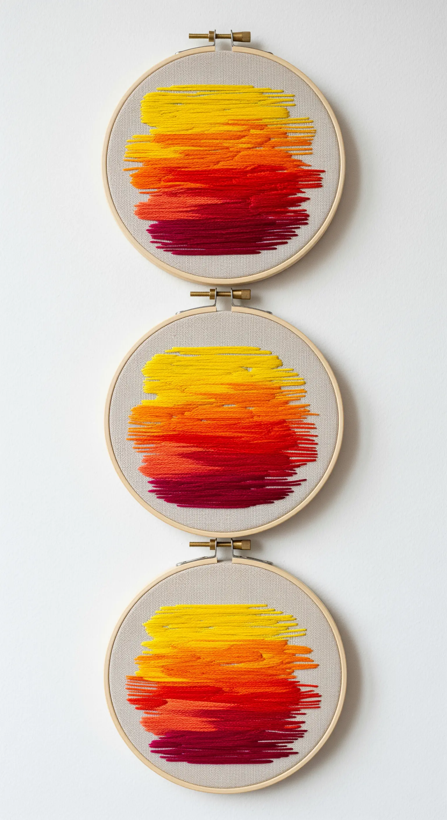 Three embroidery hoops with abstract sunset gradients in red, orange, and yellow.