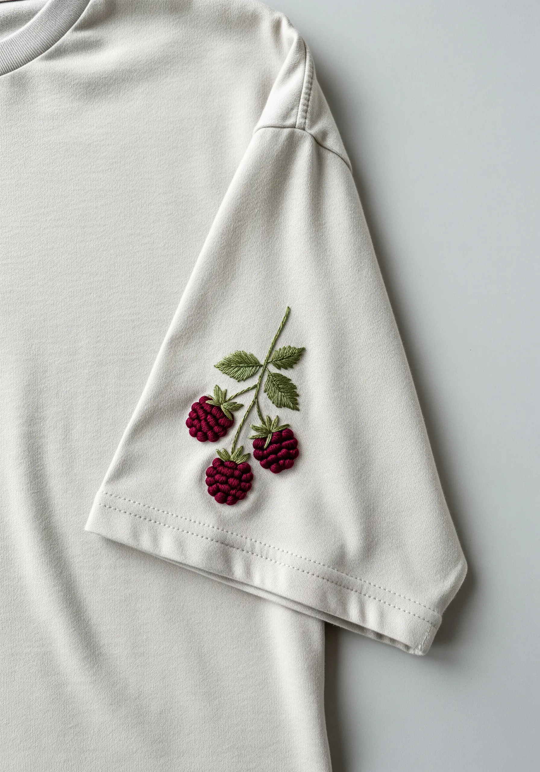 Embroidered raspberries made with French knots on the sleeve of an off-white t-shirt.